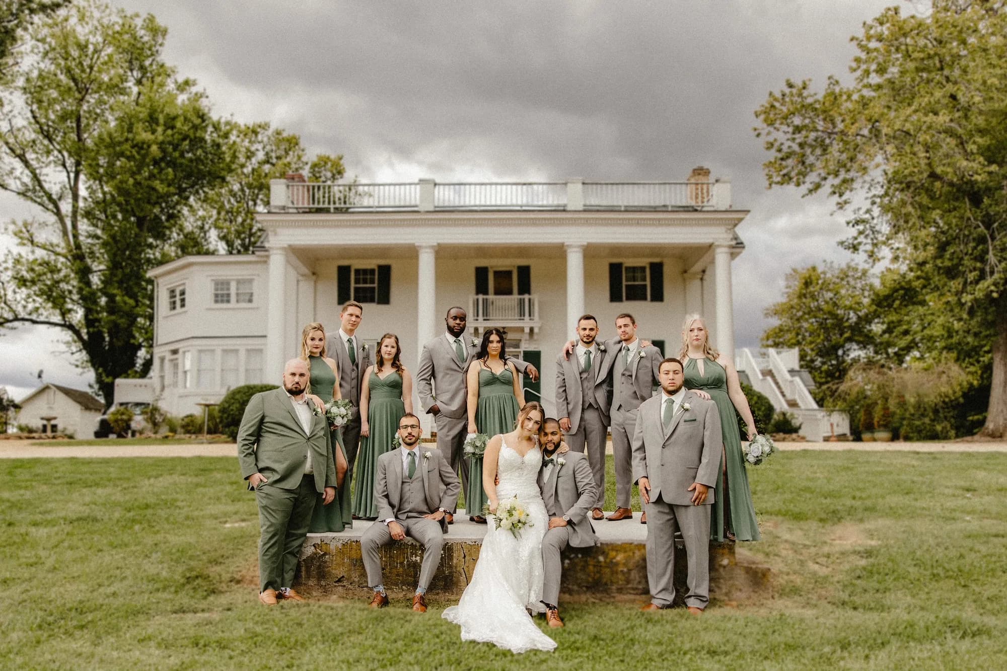 Wedding party poses on the lawn in front of Rixey Manor's white colonial facade under dramatic storm clouds