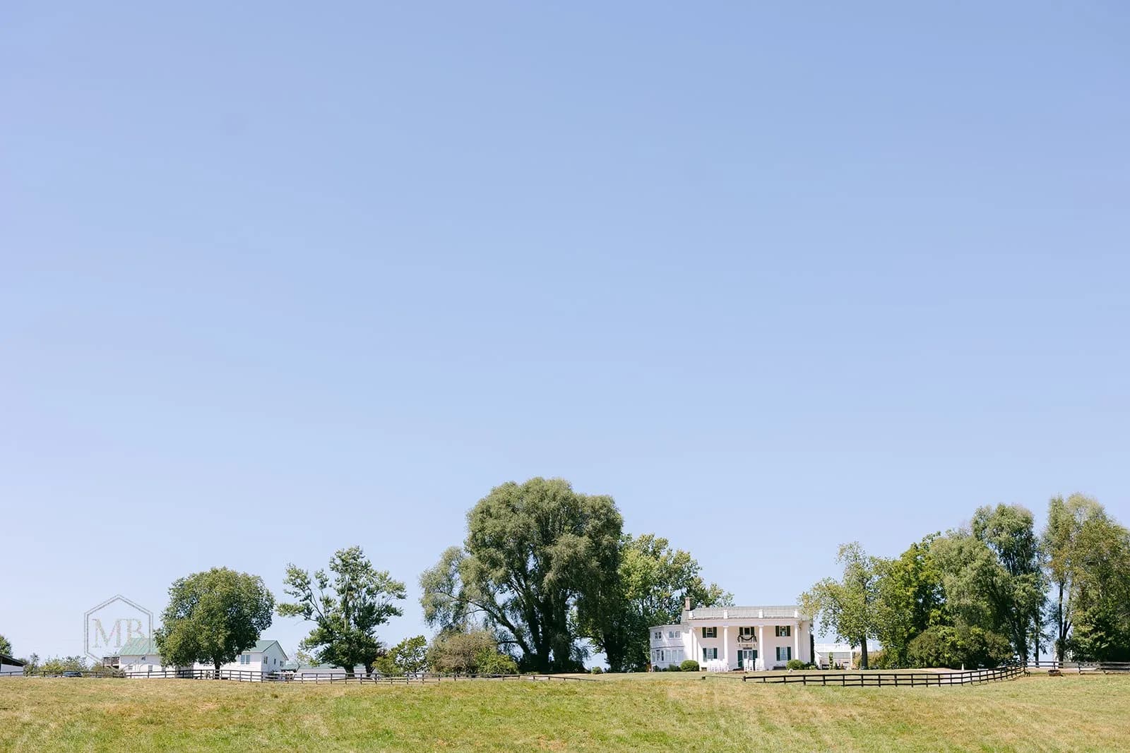 Wide establishing shot of Rixey Manor estate amid green fields and tall trees under a clear blue sky