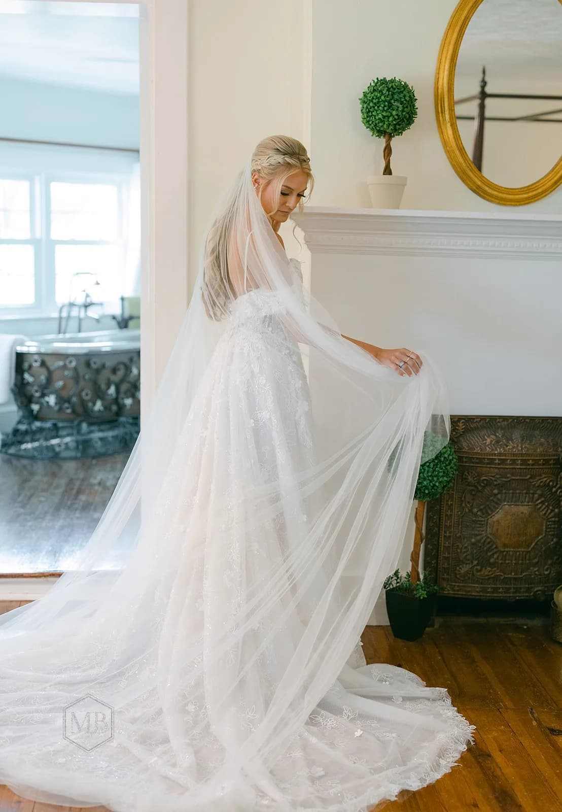 Bride in flowing white gown with veil poses by fireplace at Rixey Manor