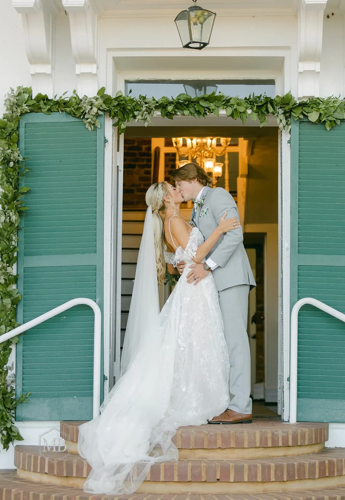 Bride and groom share a kiss in the doorway of Rixey Manor's columned entrance draped in greenery garland