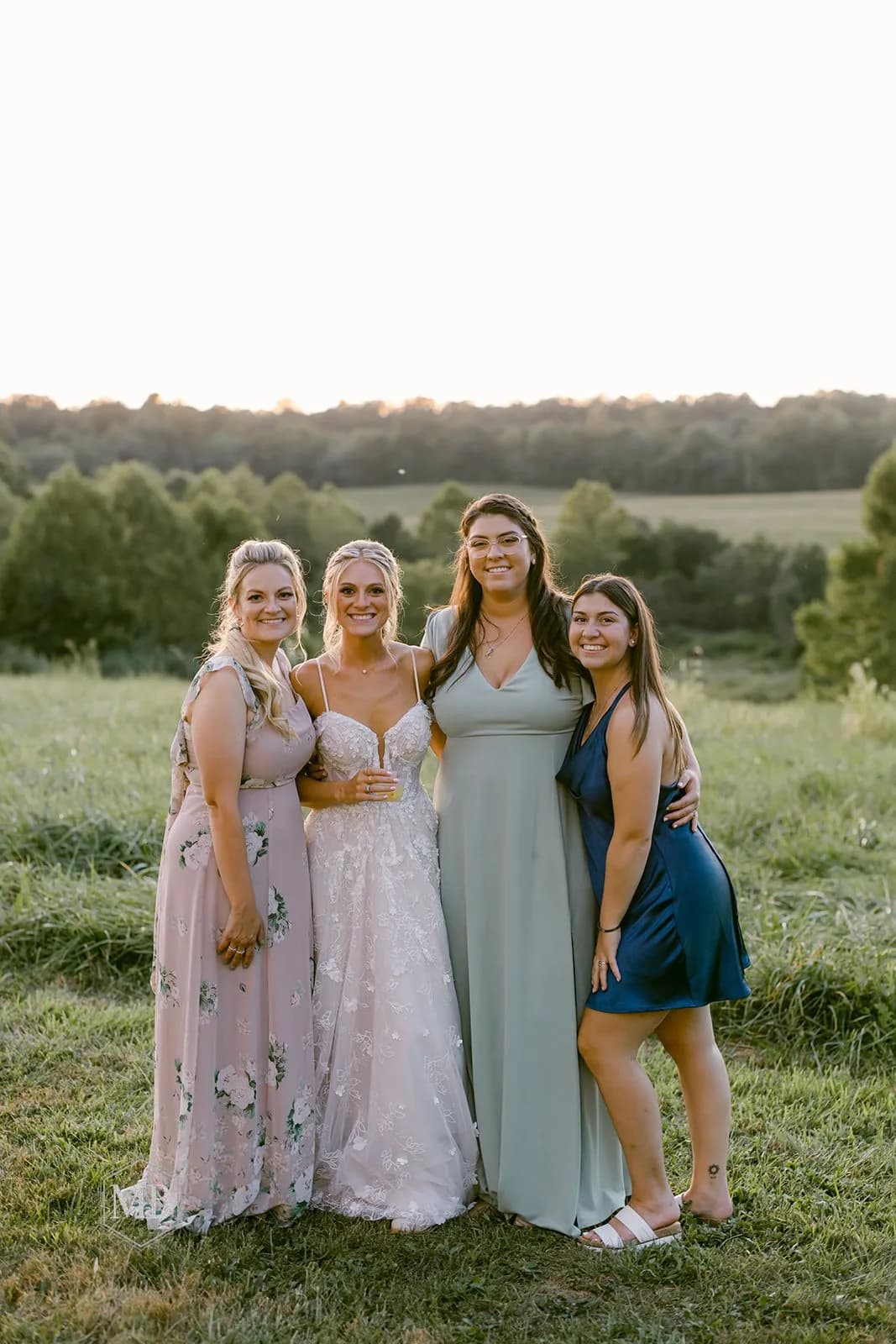 Bride and three friends laughing together in golden hour light on the green grounds of Rixey Manor