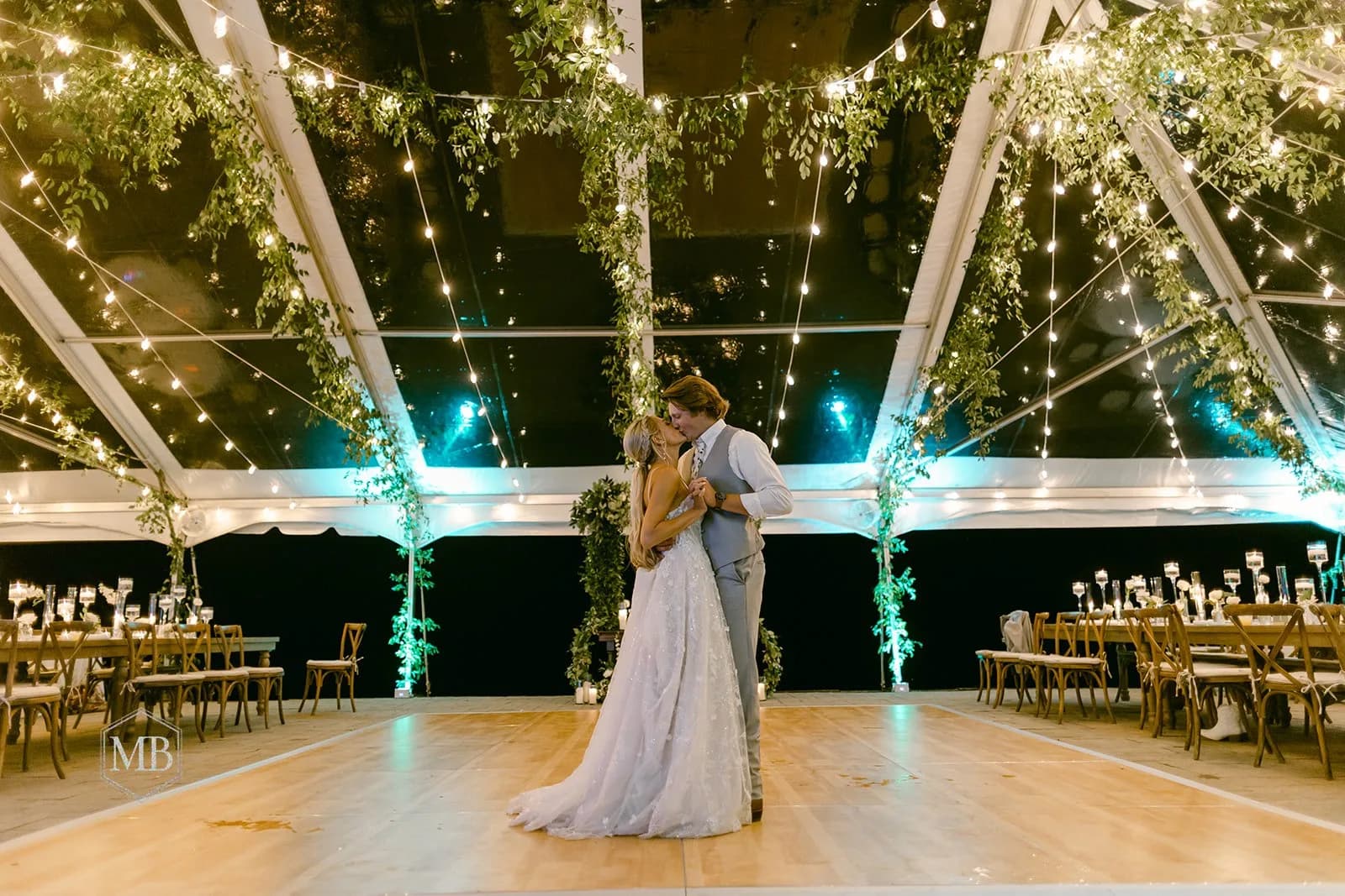 Bride and groom share first dance under string lights and greenery in Rixey Manor's tented reception pavilion