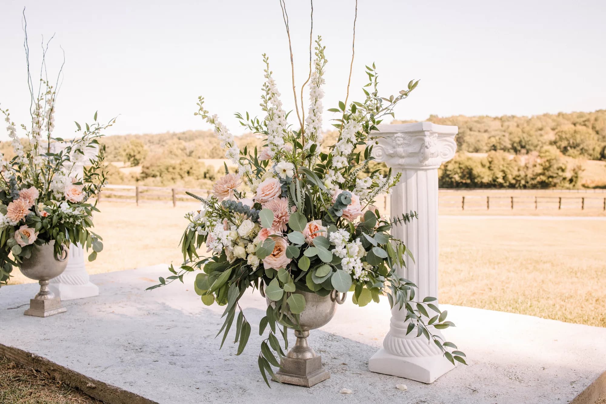 Lush floral arrangements in stone urns on white marble altar overlooking Rixey Manor's sunlit pastoral grounds