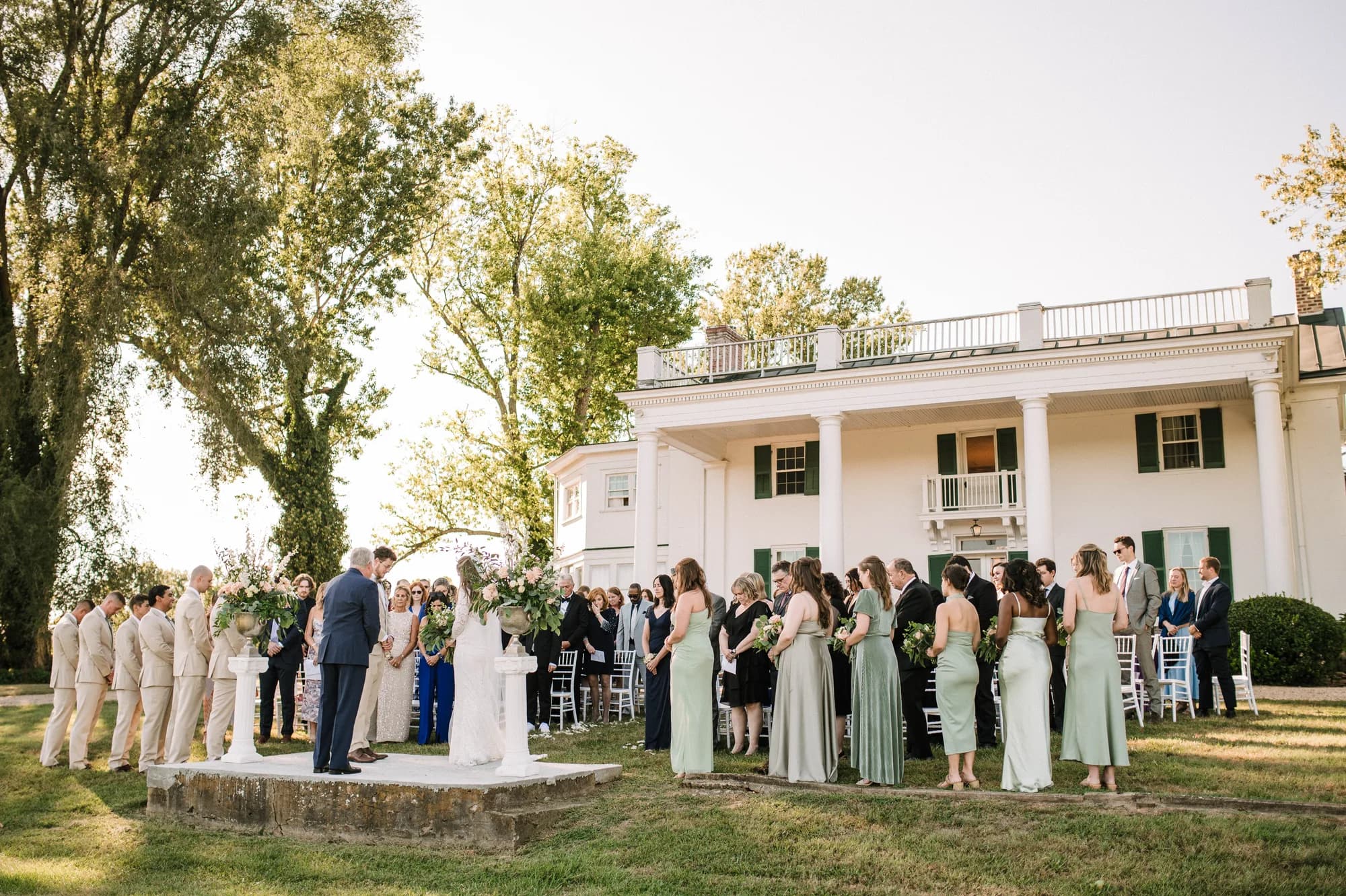 Outdoor wedding ceremony at Rixey Manor with guests gathered under a pergola, white manor visible in background