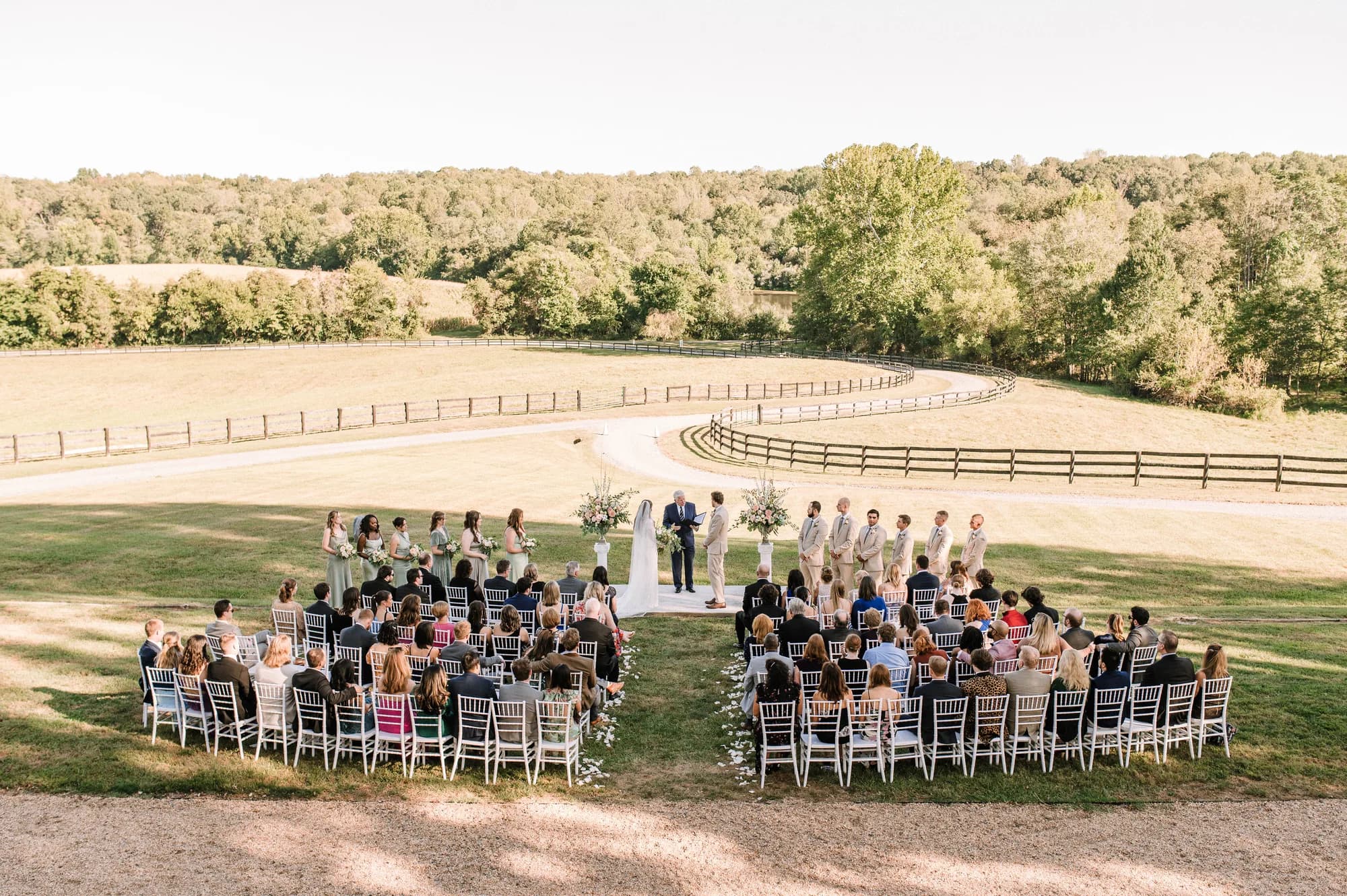 Aerial view of outdoor wedding ceremony on Rixey Manor's sunlit grounds with rolling fields and tree line behind