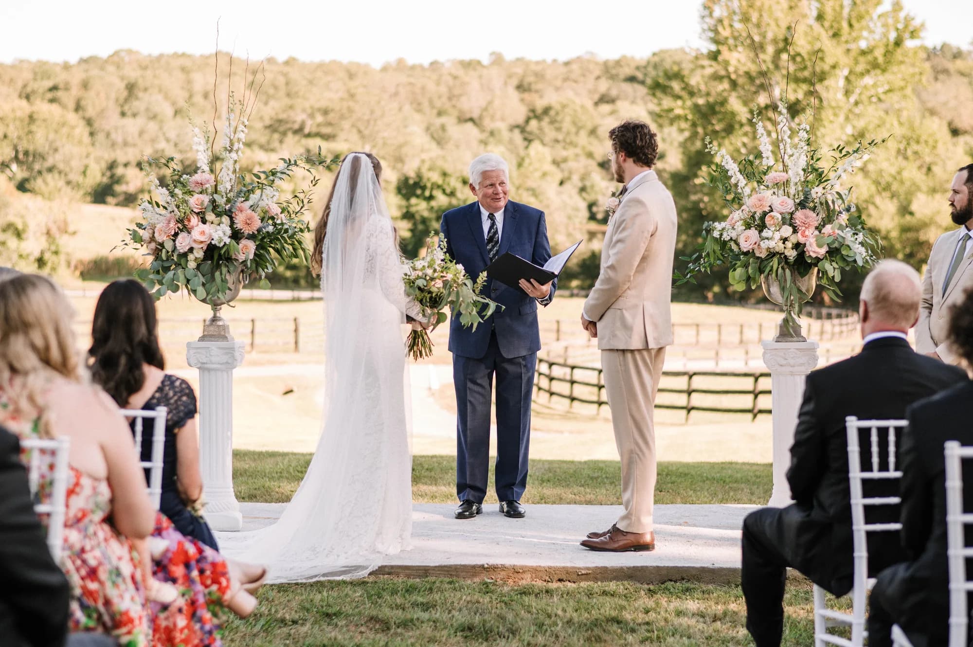 Bride and groom exchange vows at outdoor ceremony flanked by floral arrangements at Rixey Manor's rolling estate grounds
