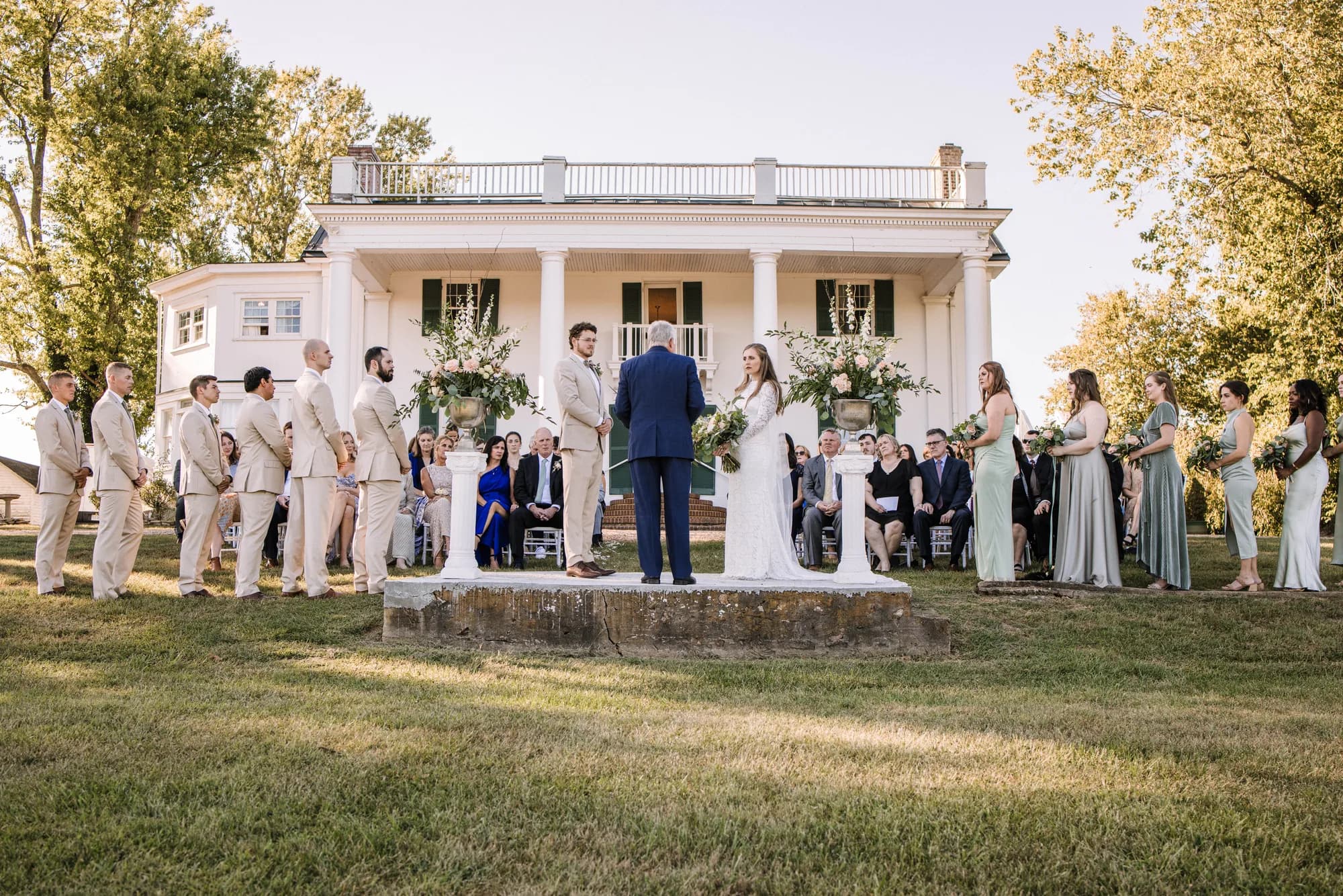 Couple exchanges vows on historic carriage steps at Rixey Manor with full wedding party and white columned manor behind