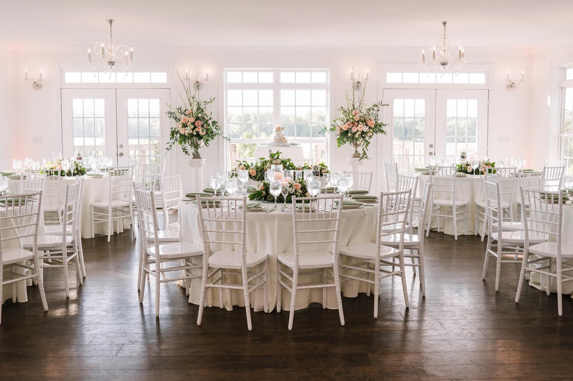 Elegant white reception hall at Rixey Manor with chiavari chairs, floral centerpieces, and cake table by French doors