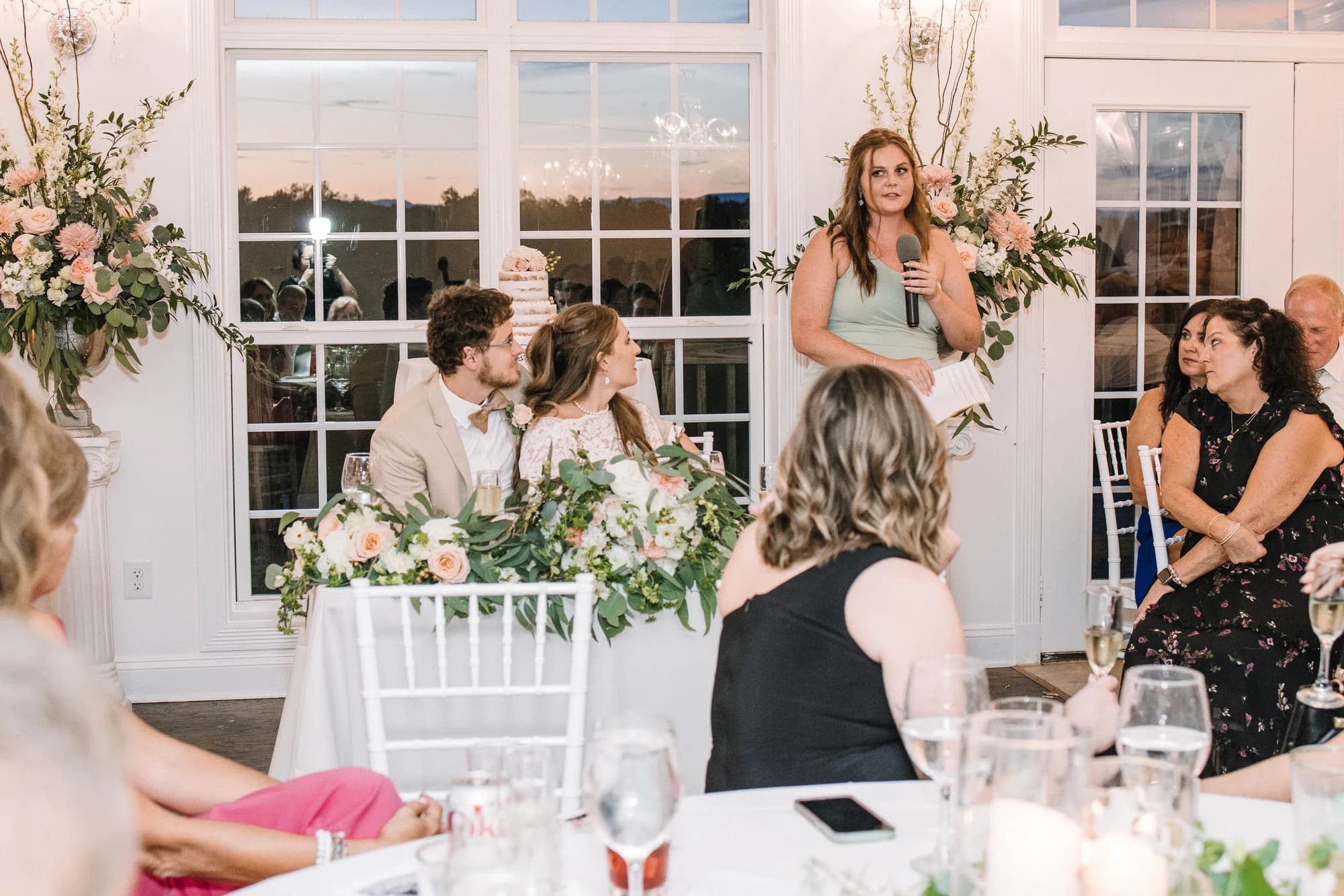 Bridesmaid delivers toast as couple leans in at sweetheart table during Rixey Manor reception
