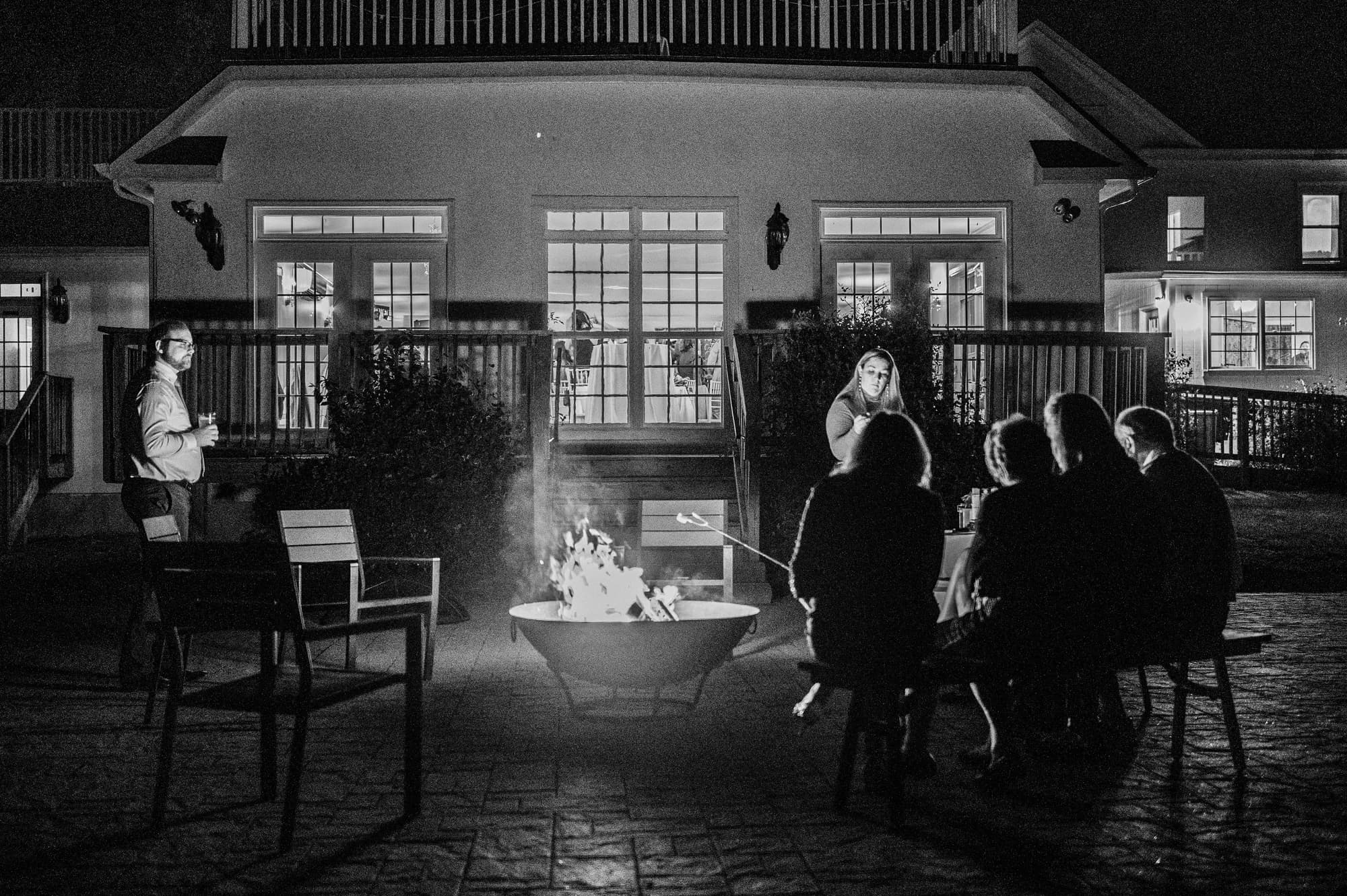 Wedding guests gather around an outdoor fire pit at night in front of Rixey Manor's illuminated facade
