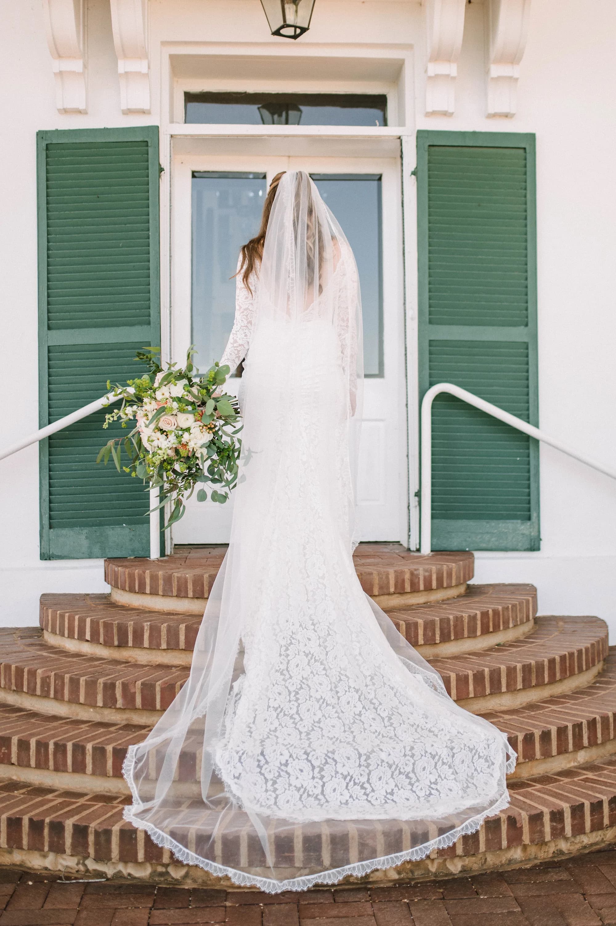 Bride in lace gown and veil stands on brick carriage steps at Rixey Manor's white columned entrance