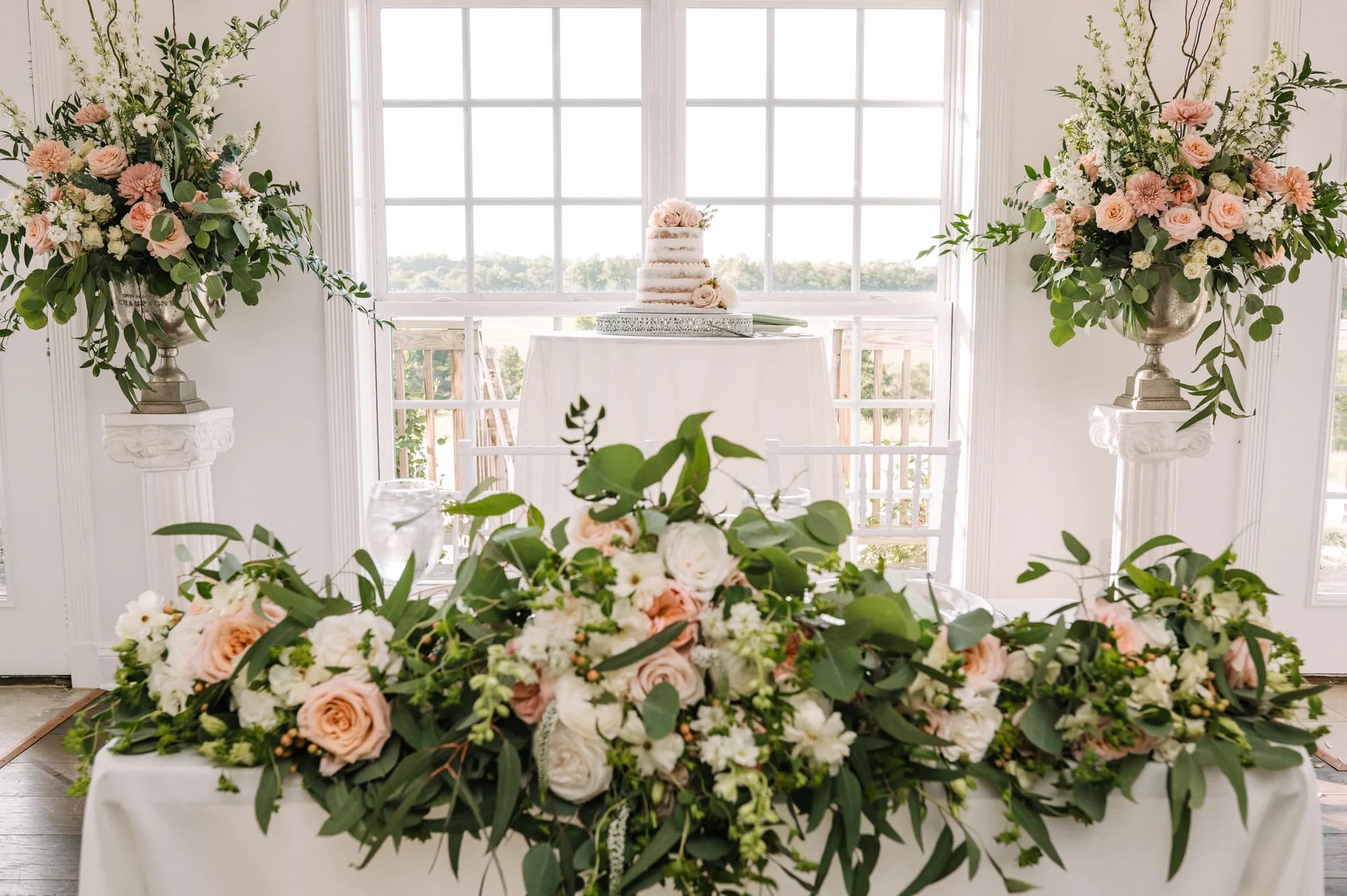 Lush blush floral arrangements and wedding cake displayed in a bright white room at Rixey Manor