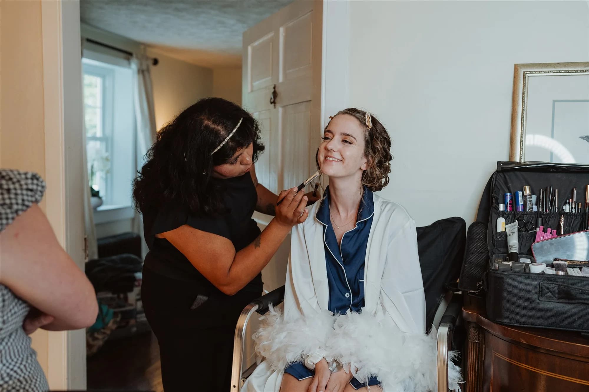 Bride smiling as makeup artist applies finishing touches in a bright getting-ready room