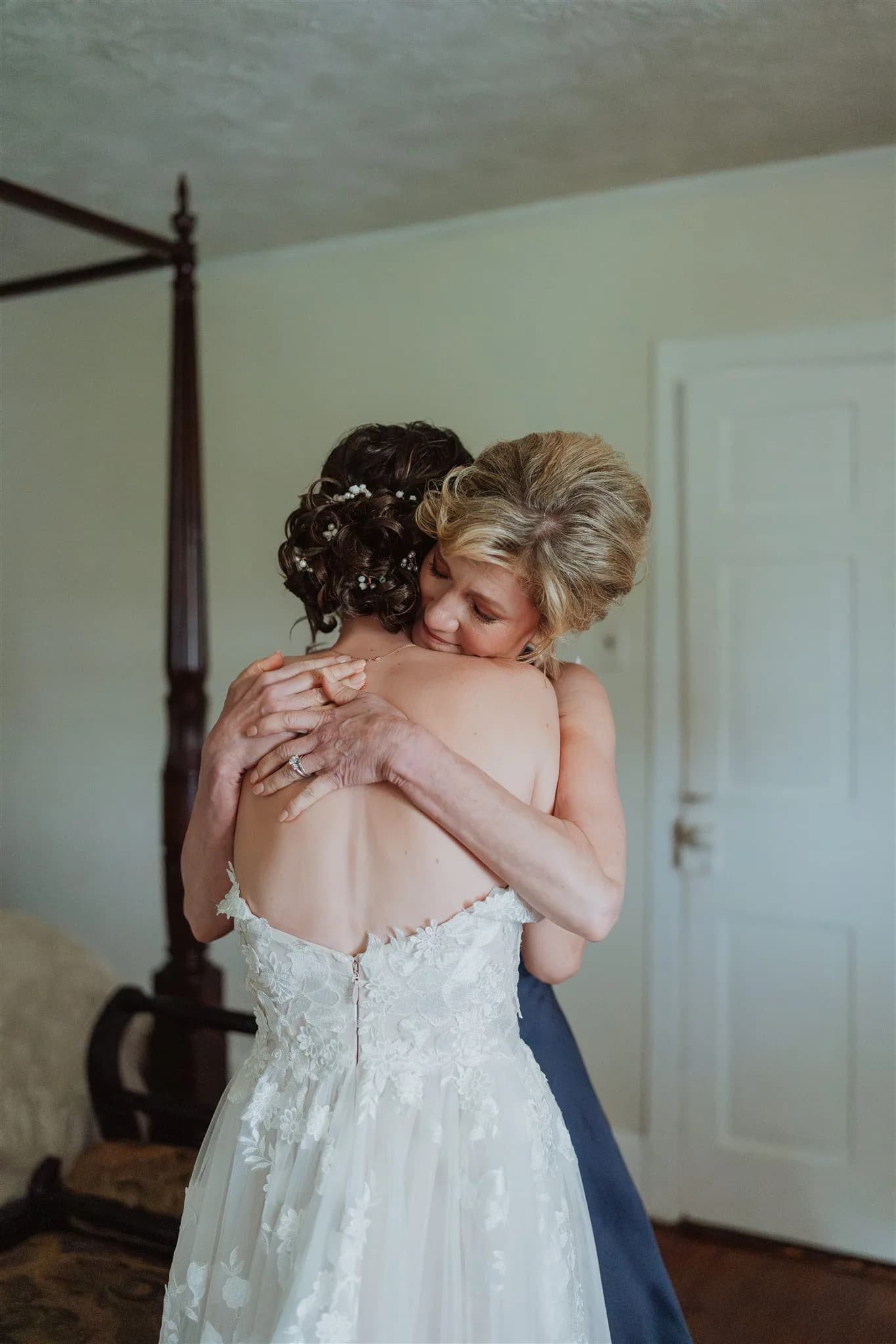 Bride and mother share a tender embrace in a sunlit room before the wedding ceremony