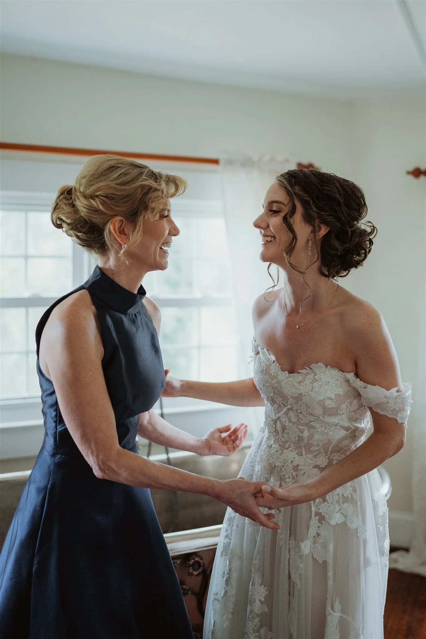 Bride and mother share a joyful laugh while getting ready in a sunlit room at Rixey Manor