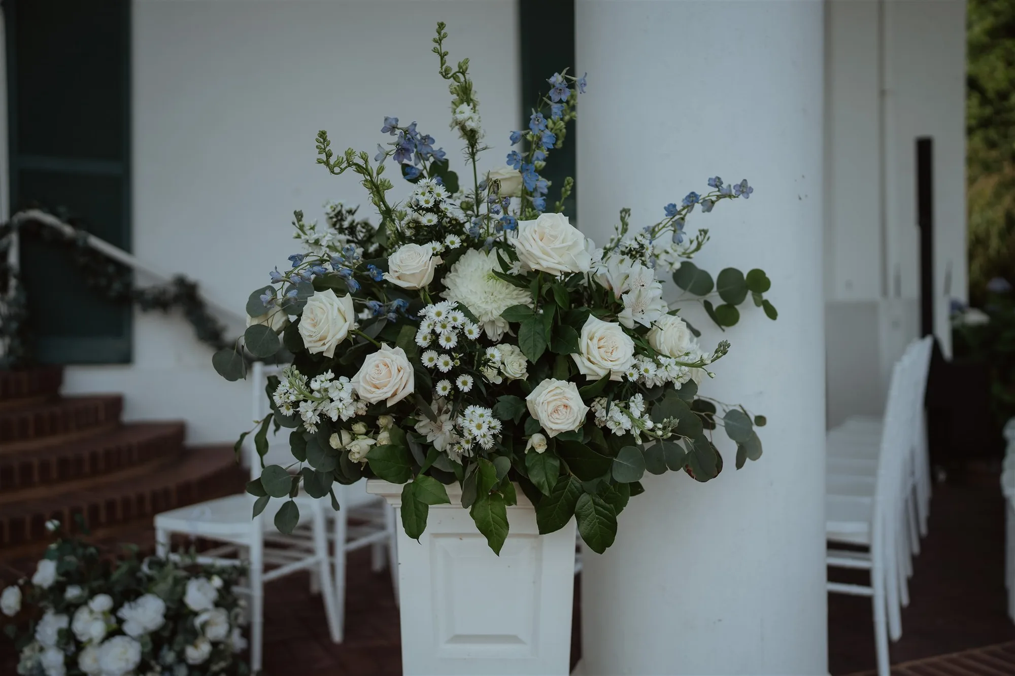 White roses and blue delphinium floral arrangement on a column at Rixey Manor outdoor ceremony site