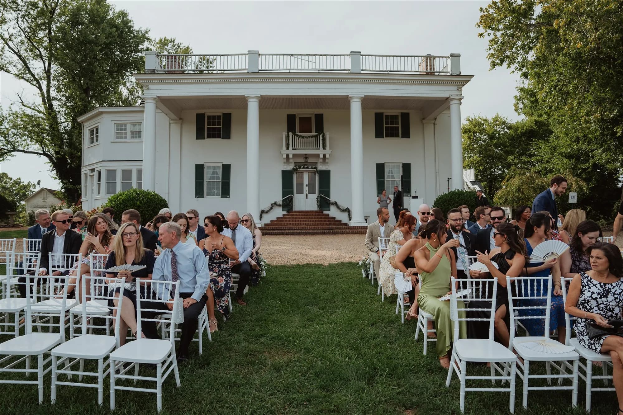 Wedding guests seated in white chairs on the lawn before Rixey Manor's grand white columned facade