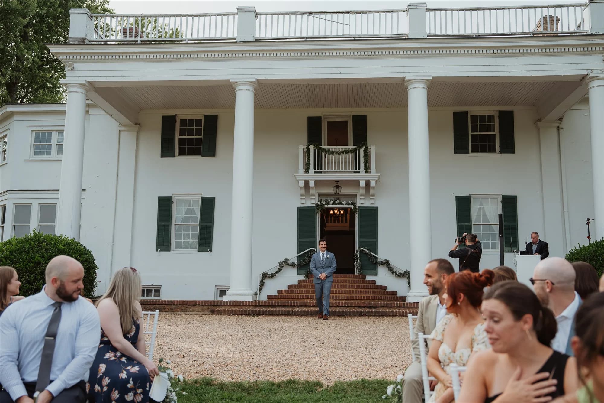 Groom walks down brick steps of Rixey Manor's white-columned estate toward seated wedding guests outdoors