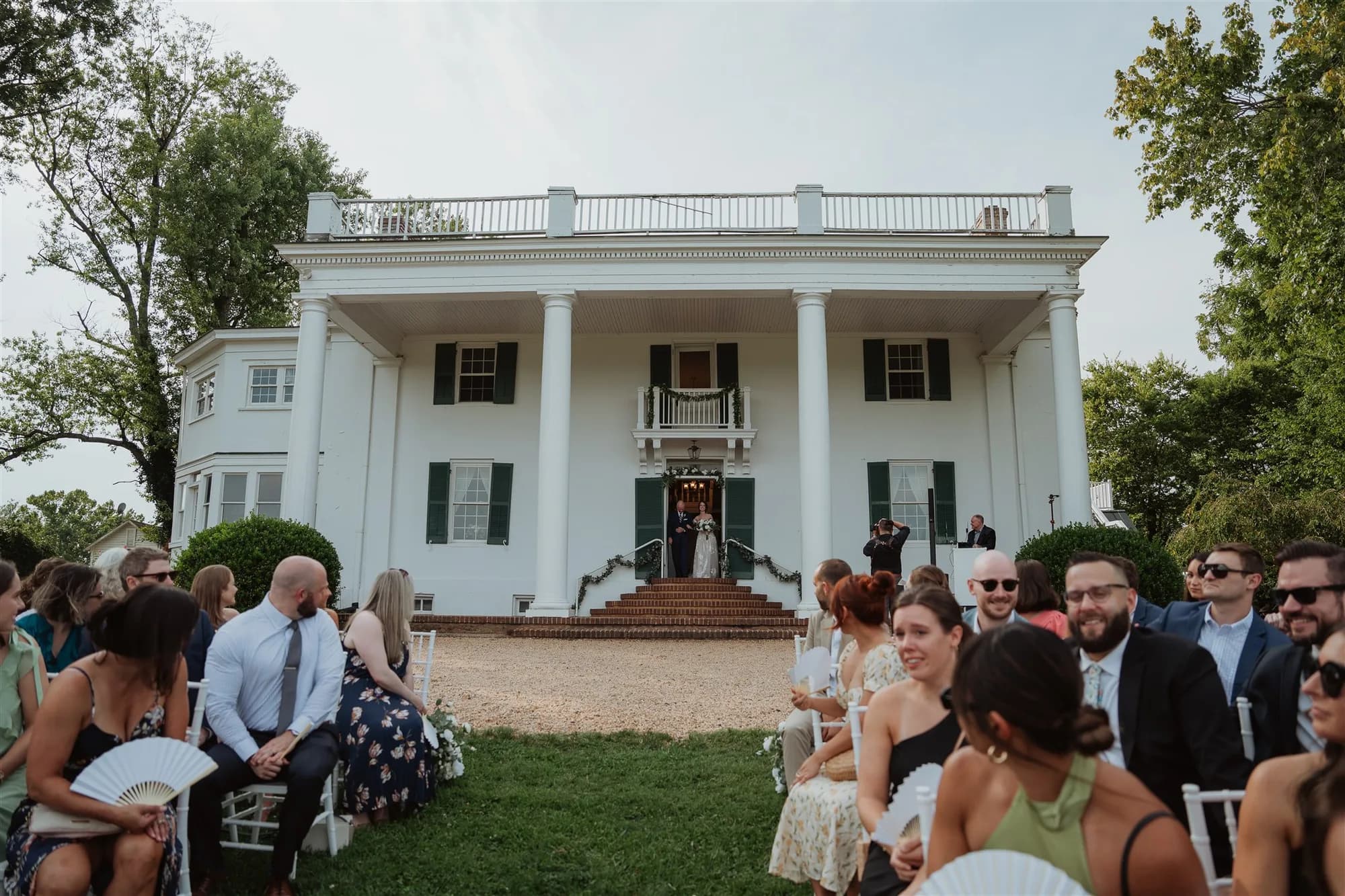 Wedding ceremony on the grand steps of Rixey Manor's white columned estate with seated guests on the lawn