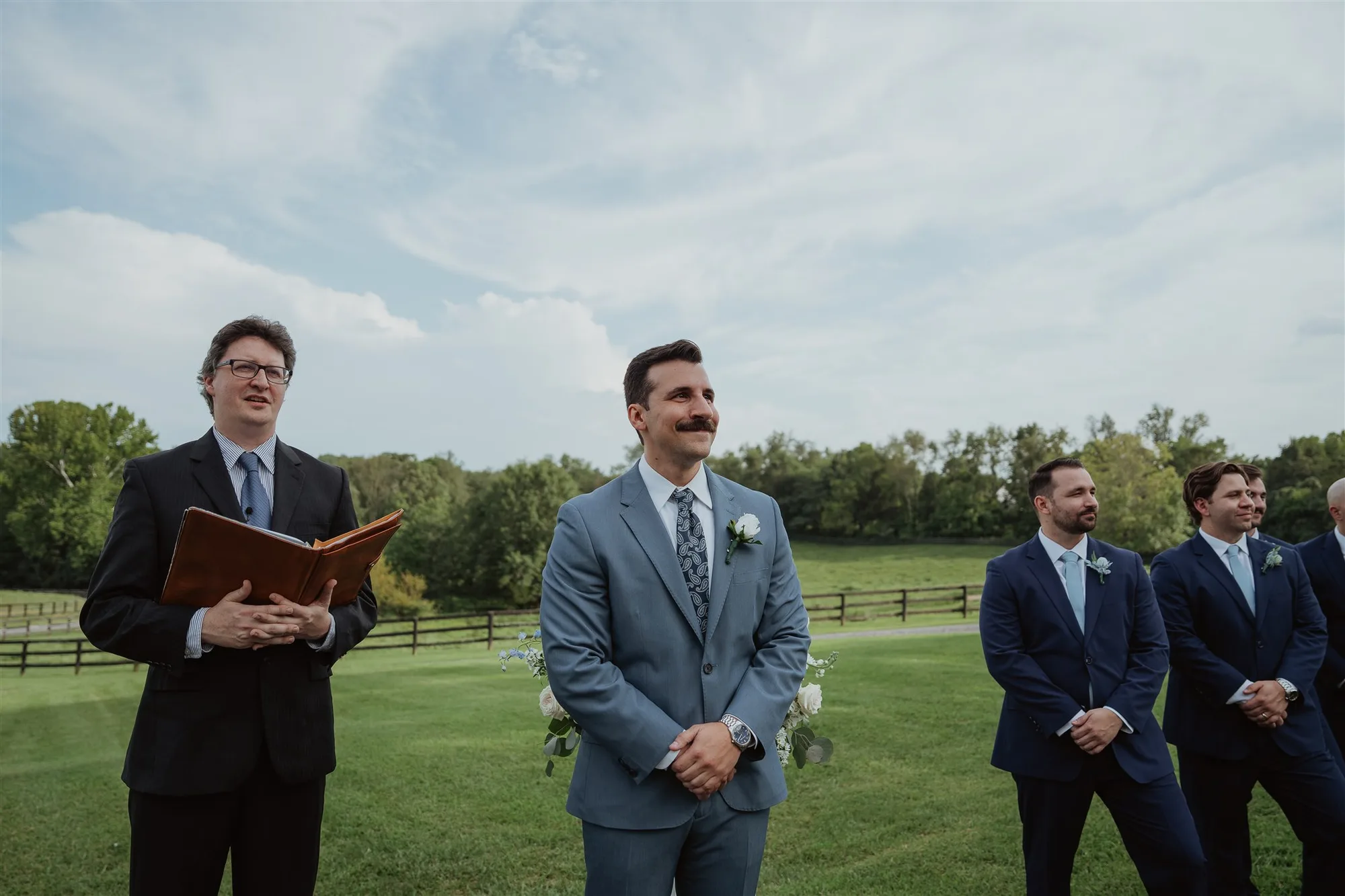 Groom smiling with anticipation at outdoor ceremony on Rixey Manor grounds with groomsmen and officiant
