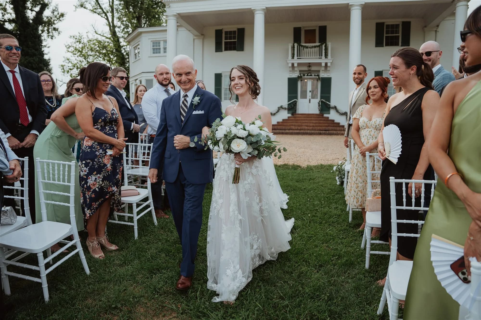 Bride and groom walking down aisle at outdoor wedding ceremony in front of white manor