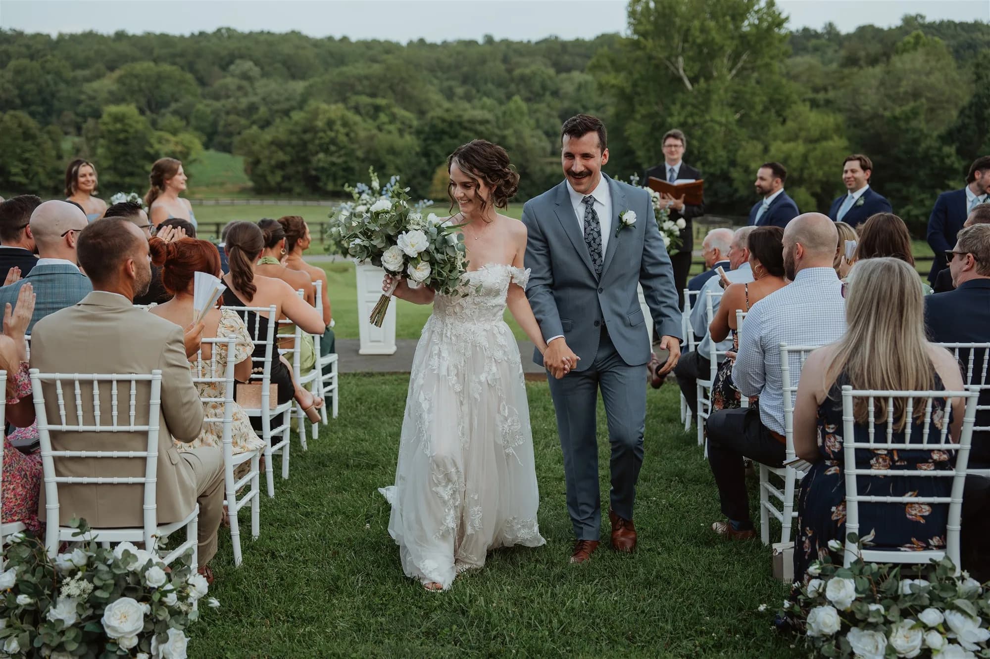 Newlyweds walk back down the aisle at Rixey Manor outdoor ceremony, rolling Virginia hills behind them
