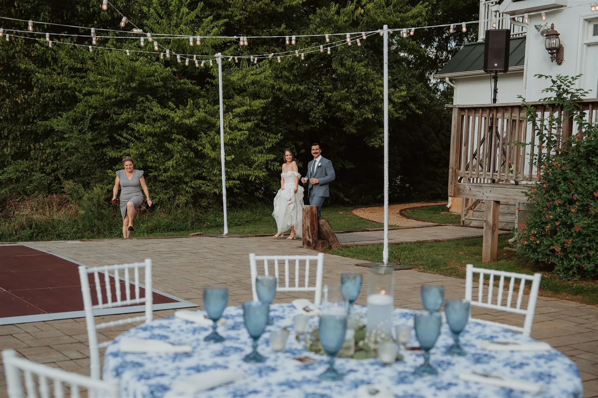 Couple makes grand entrance onto Rixey Manor's outdoor patio reception with string lights and blue-accented tablescapes
