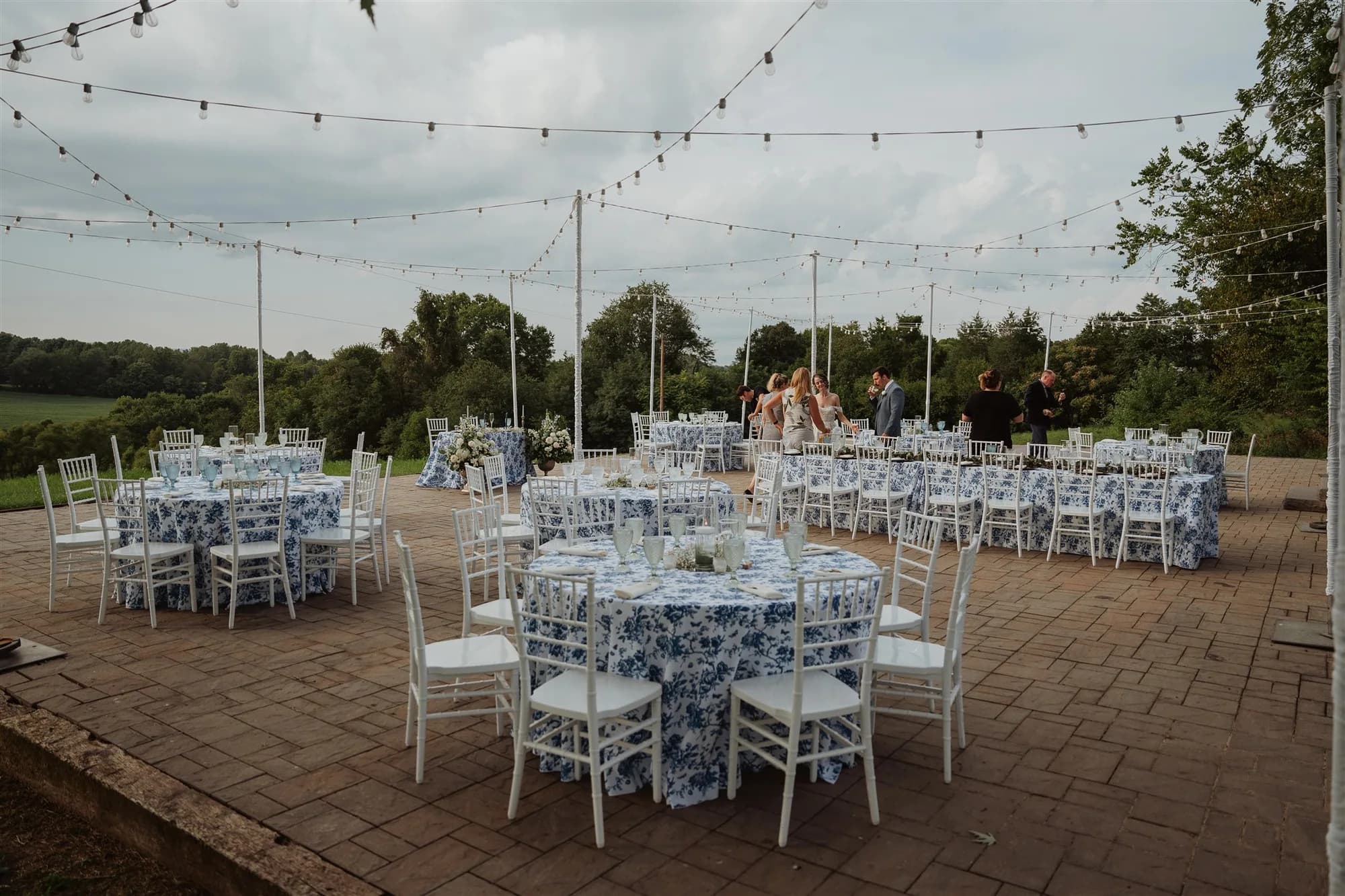 Blue floral tablecloths on round tables set for an outdoor reception on the Rixey Manor terrace with string lights