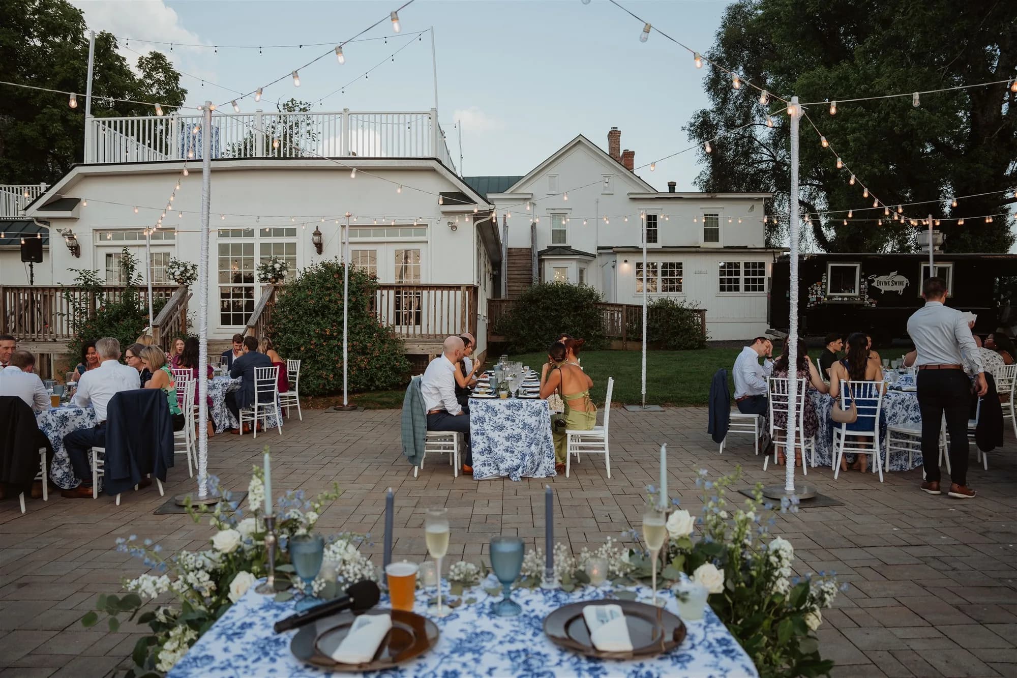 Outdoor evening wedding reception on Rixey Manor patio with string lights, floral tables, and white estate backdrop