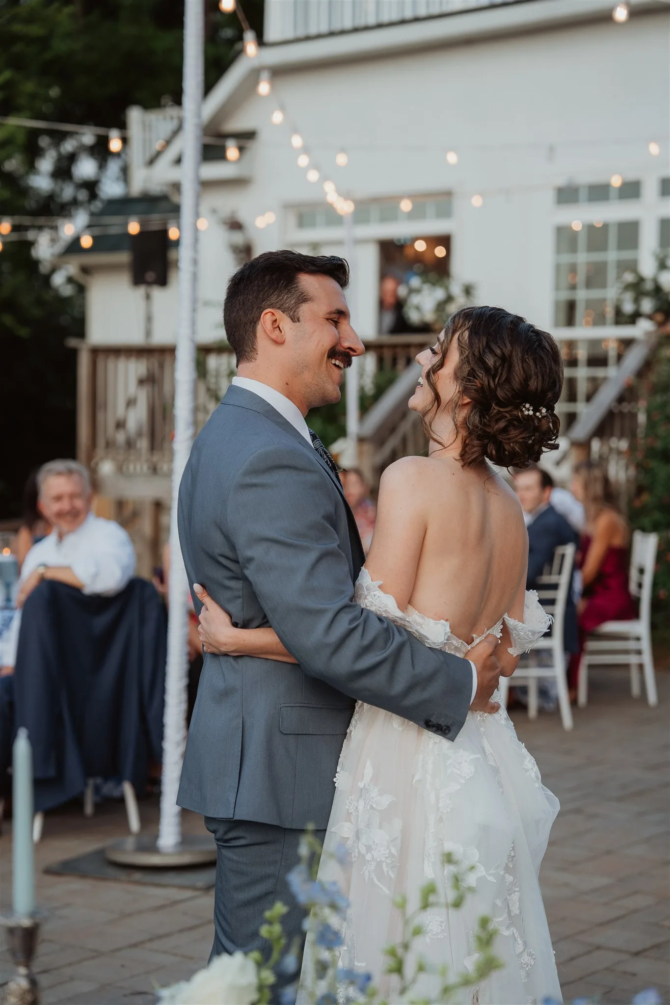 Bride and groom share a joyful first dance on the Rixey Manor outdoor terrace under string lights at dusk