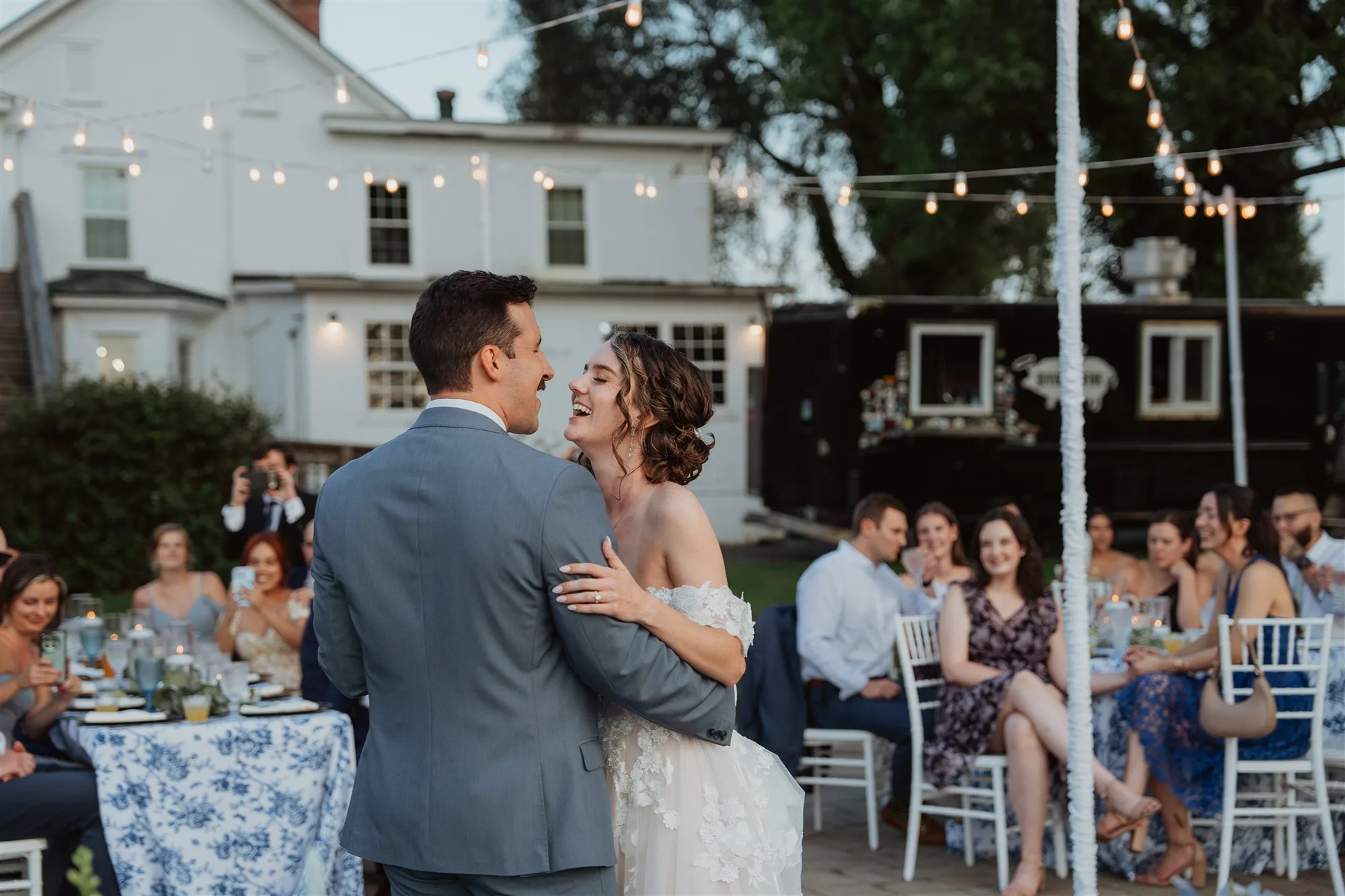 Bride and groom share a joyful first dance under string lights at Rixey Manor outdoor reception at dusk