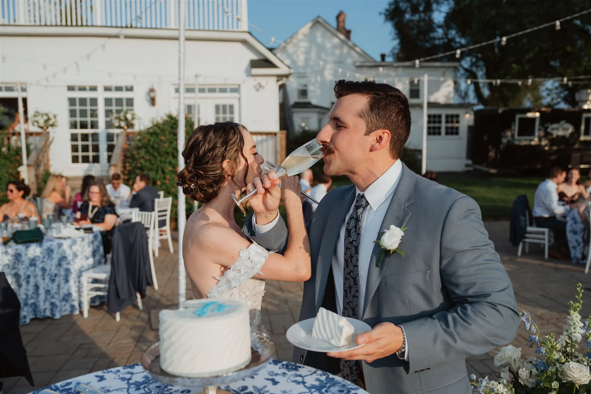 Bride and groom share champagne and wedding cake on the terrace at Rixey Manor during outdoor reception