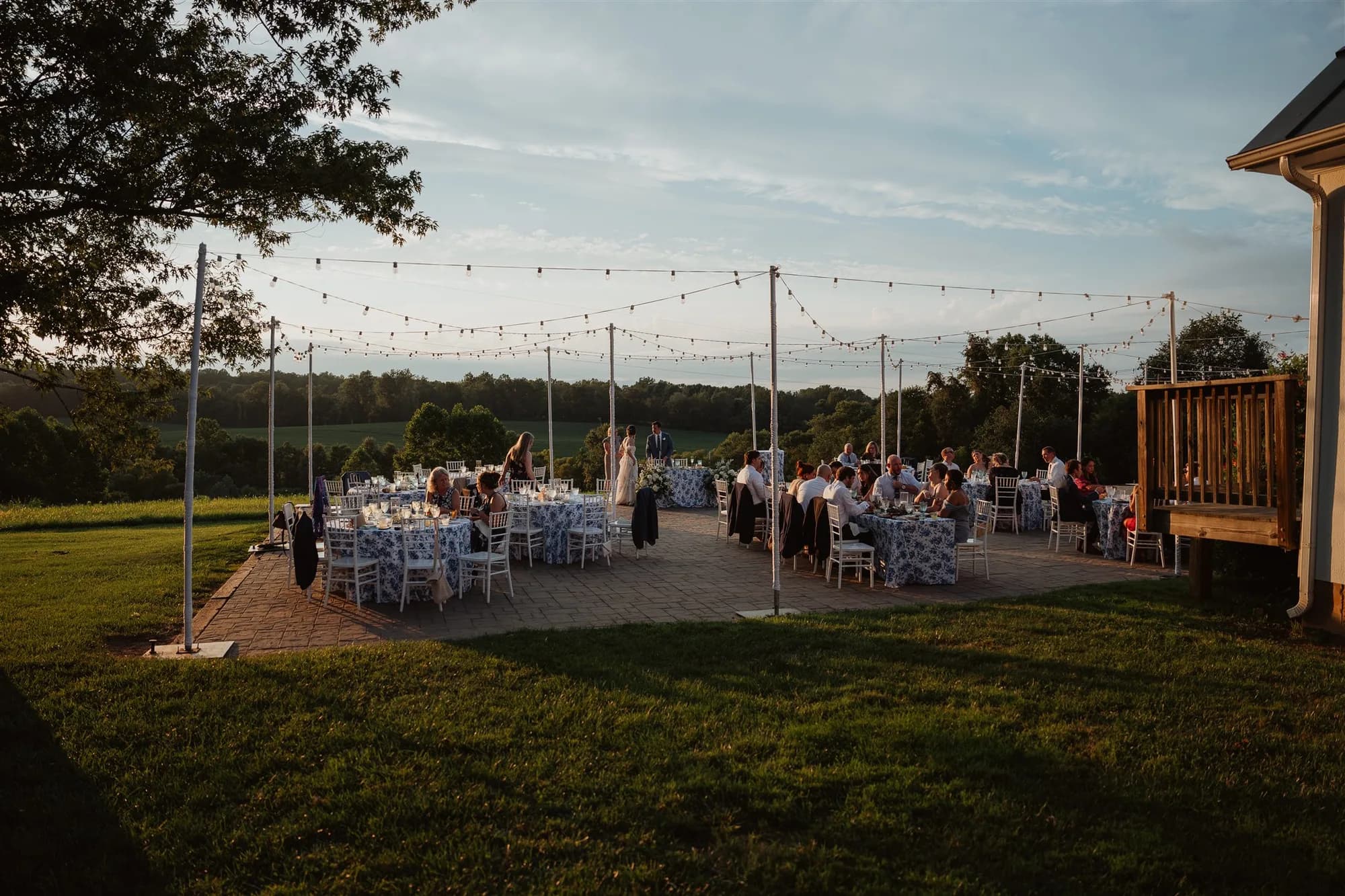 Outdoor wedding reception at golden hour with string lights over round tables on a rural Virginia estate patio
