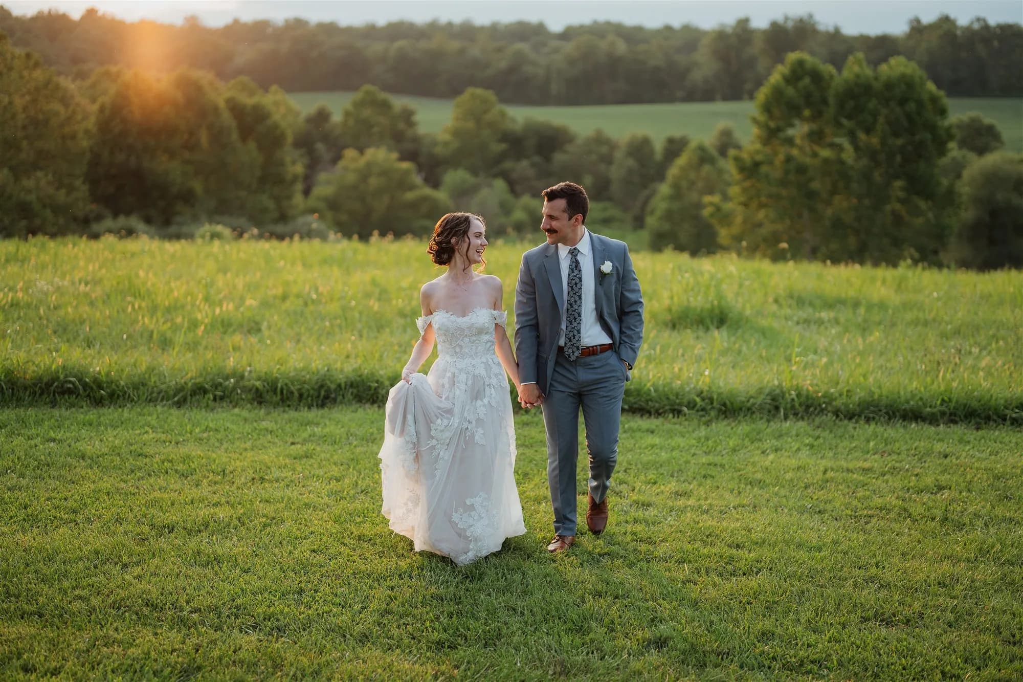 Bride and groom walk hand-in-hand through golden-hour fields at Rixey Manor, gazing at each other