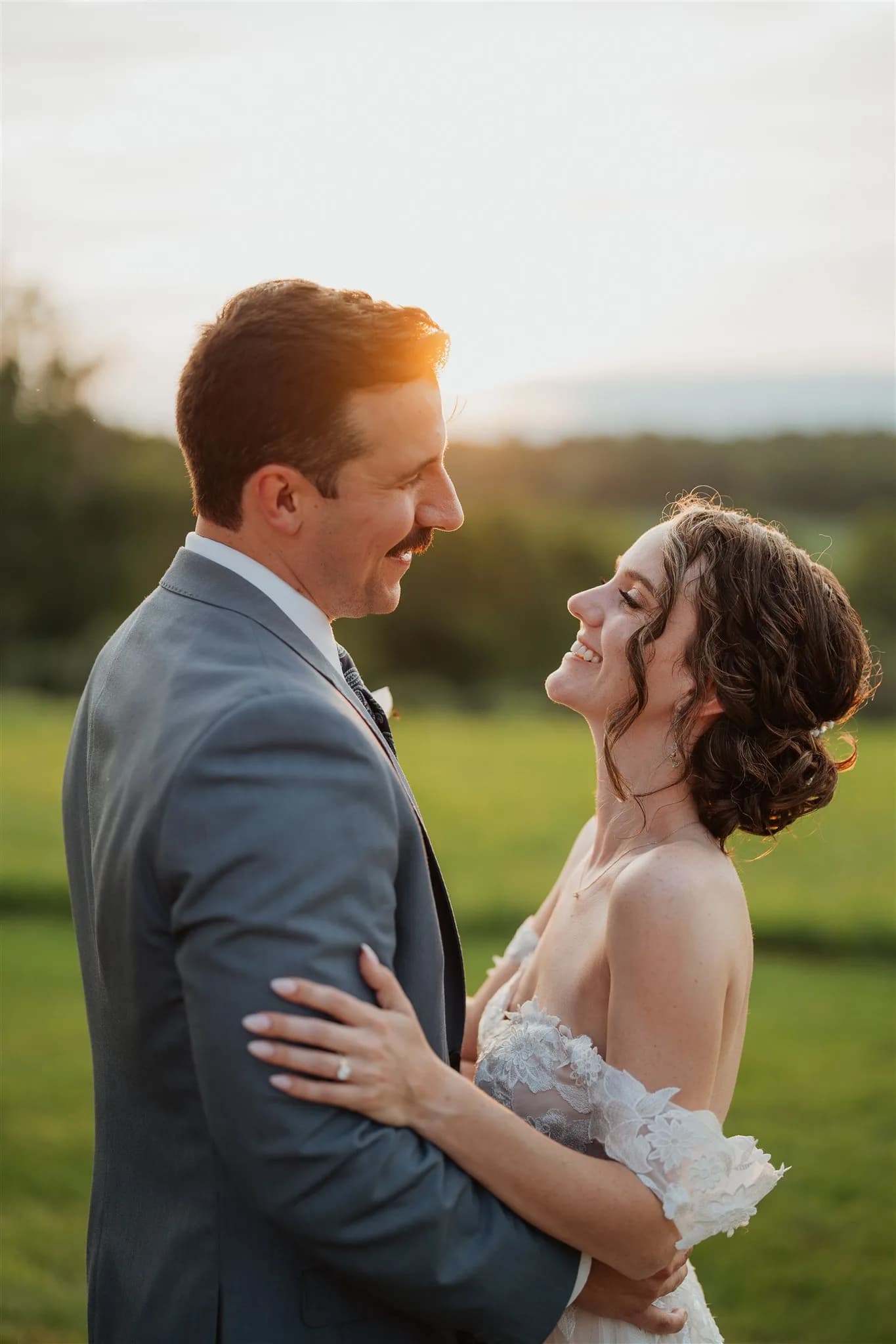 Bride laughing up at groom during golden hour portraits on lush green grounds