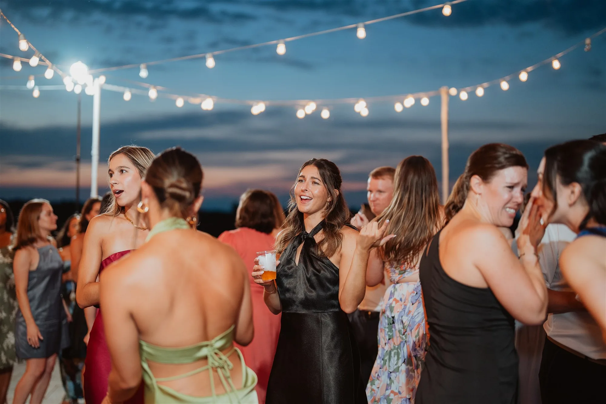 Guests laughing and dancing under string lights at an outdoor evening wedding reception at dusk