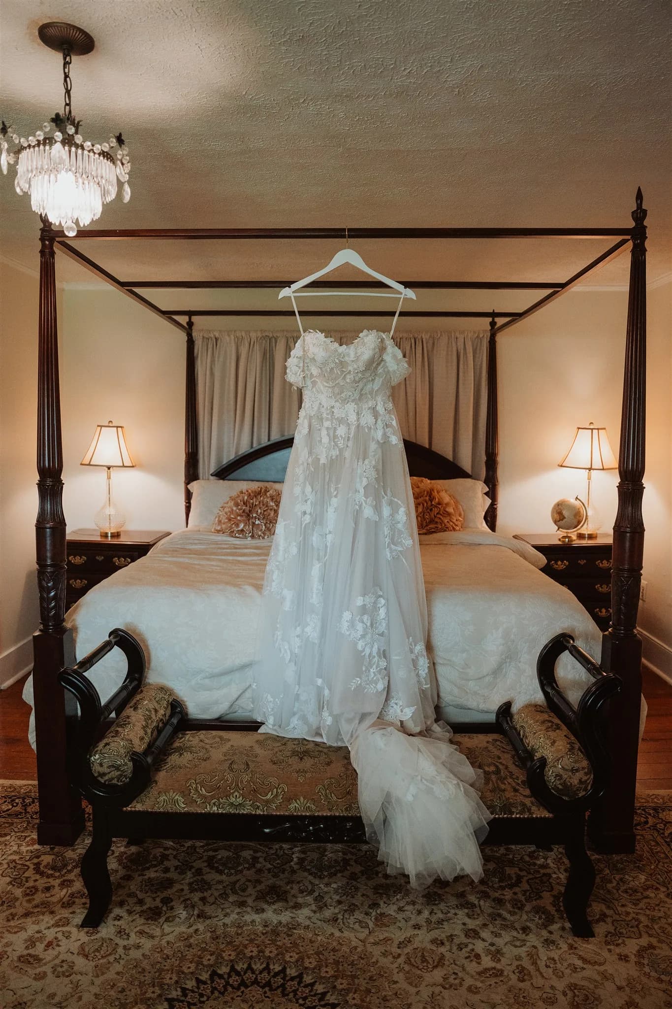 Lace wedding gown hanging from a four-poster bed in a warmly lit historic bedroom at Rixey Manor