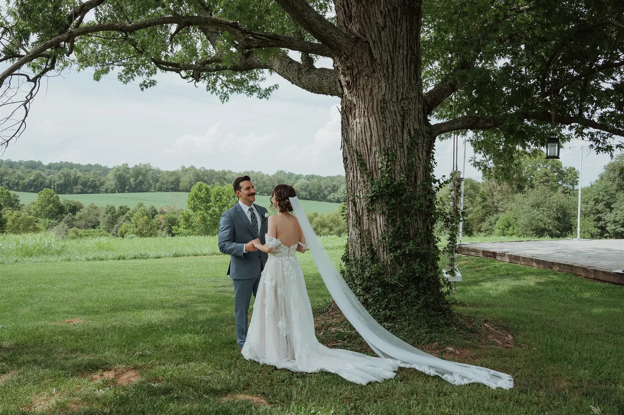 Bride and groom share a first look beneath a grand oak tree on Rixey Manor's lush green grounds