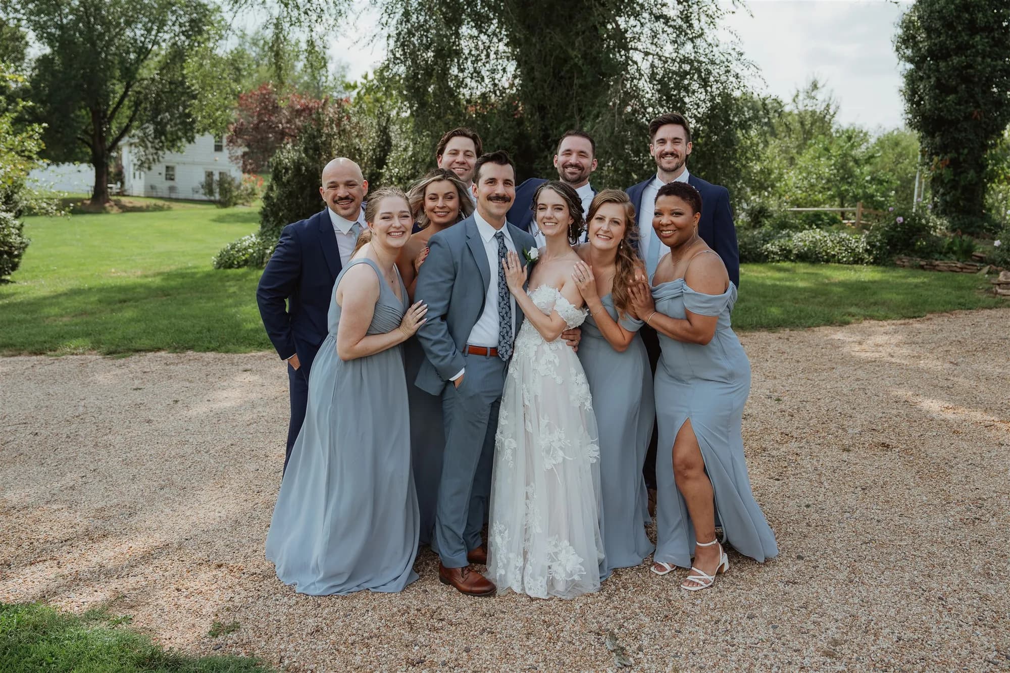 Bride and groom surrounded by smiling wedding party in blue on Rixey Manor grounds