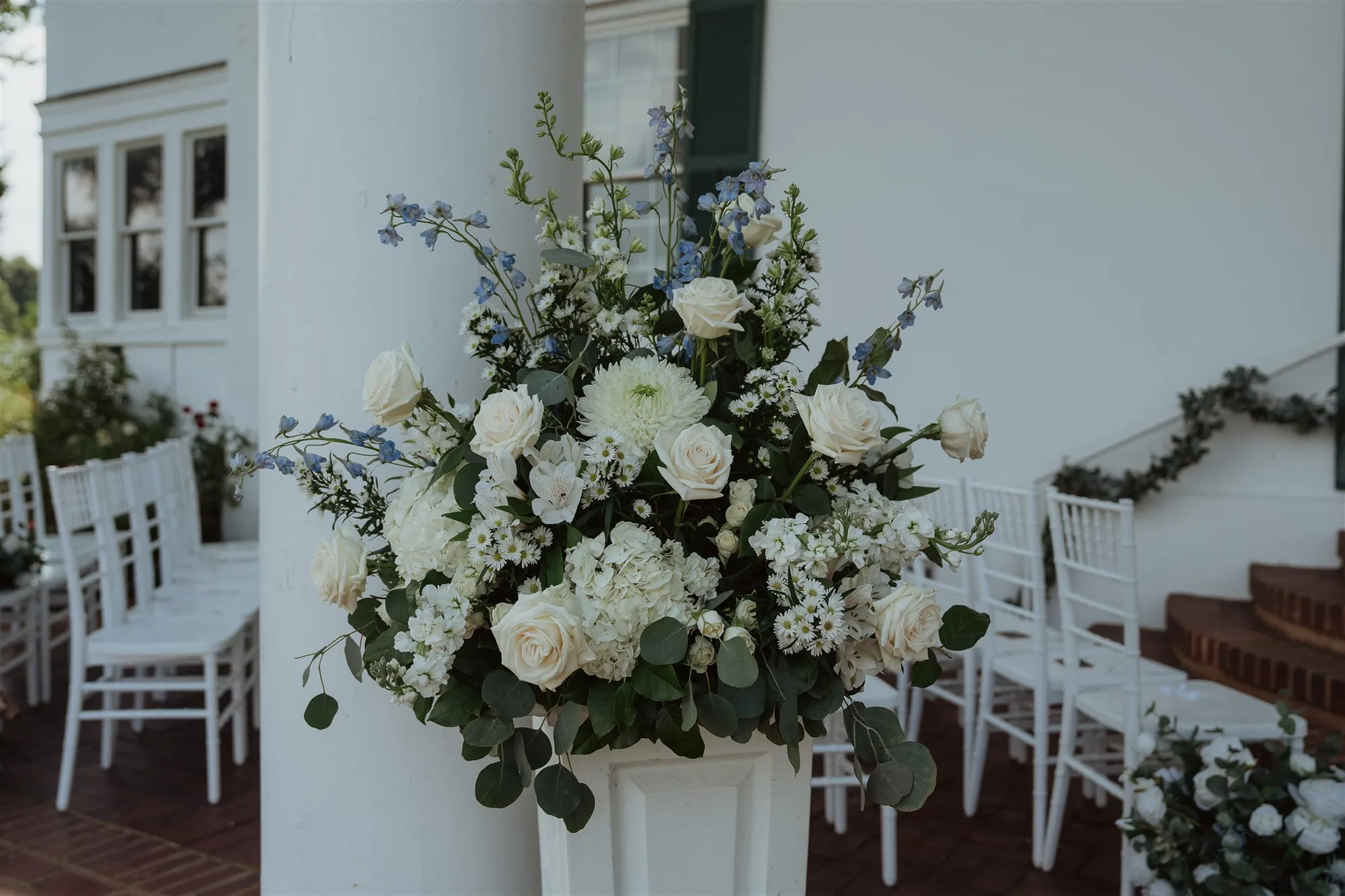 Lush white rose and blue delphinium floral arrangement on column at Rixey Manor outdoor ceremony site