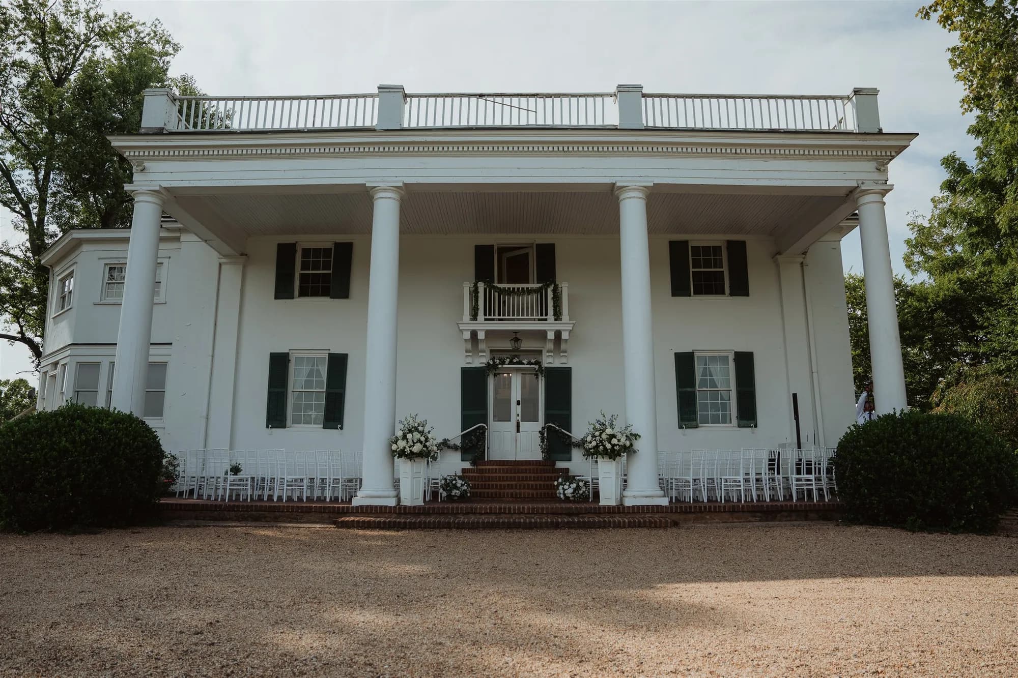 Rixey Manor's white antebellum facade with grand columns, floral arrangements, and white chairs set for a ceremony