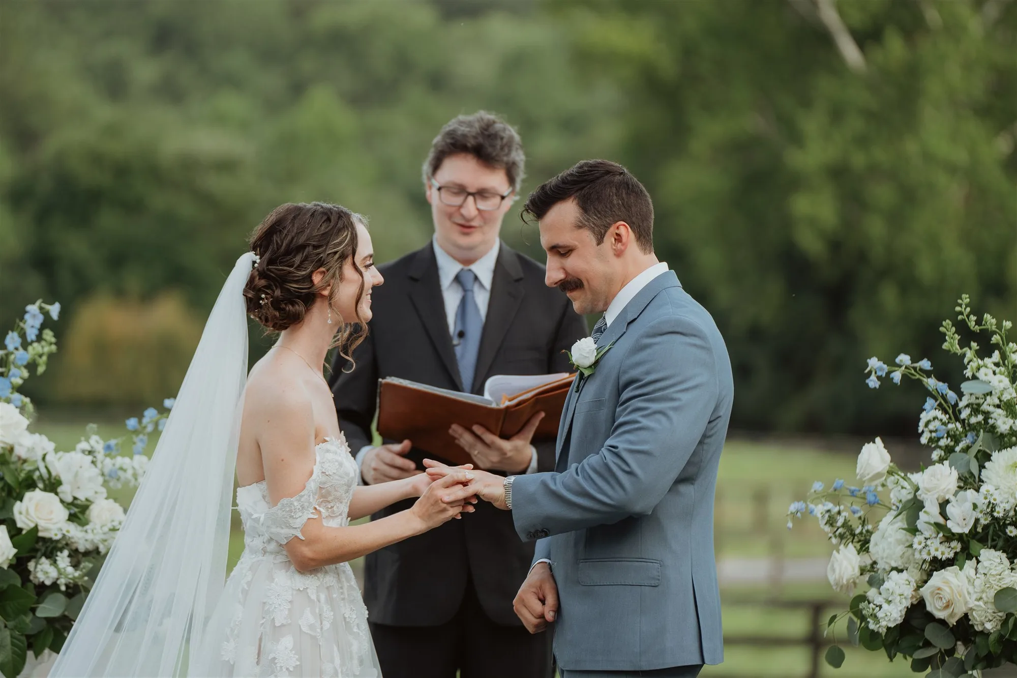 Bride and groom exchange vows during outdoor wedding ceremony with officiant holding book