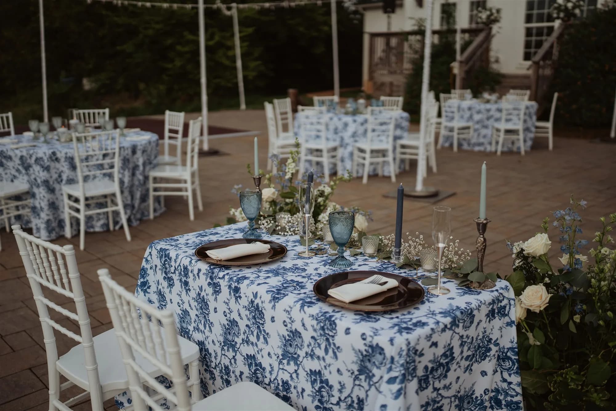 Elegant outdoor reception at Rixey Manor with blue floral linens, taper candles, and white Chiavari chairs on brick terrace