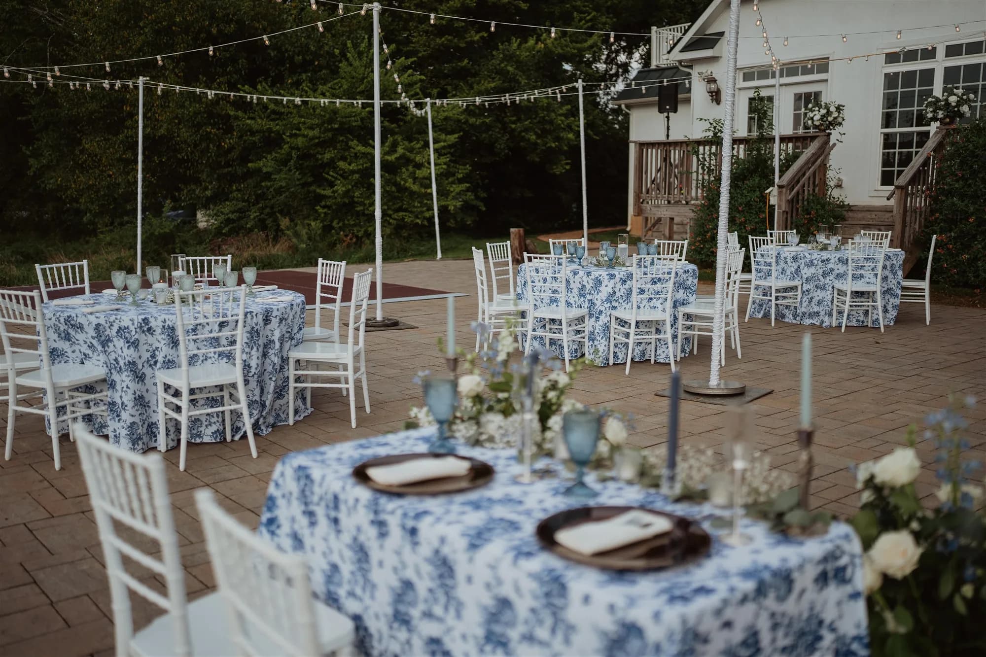 Outdoor reception tables with blue floral linens and candles on brick patio at Rixey Manor, Virginia