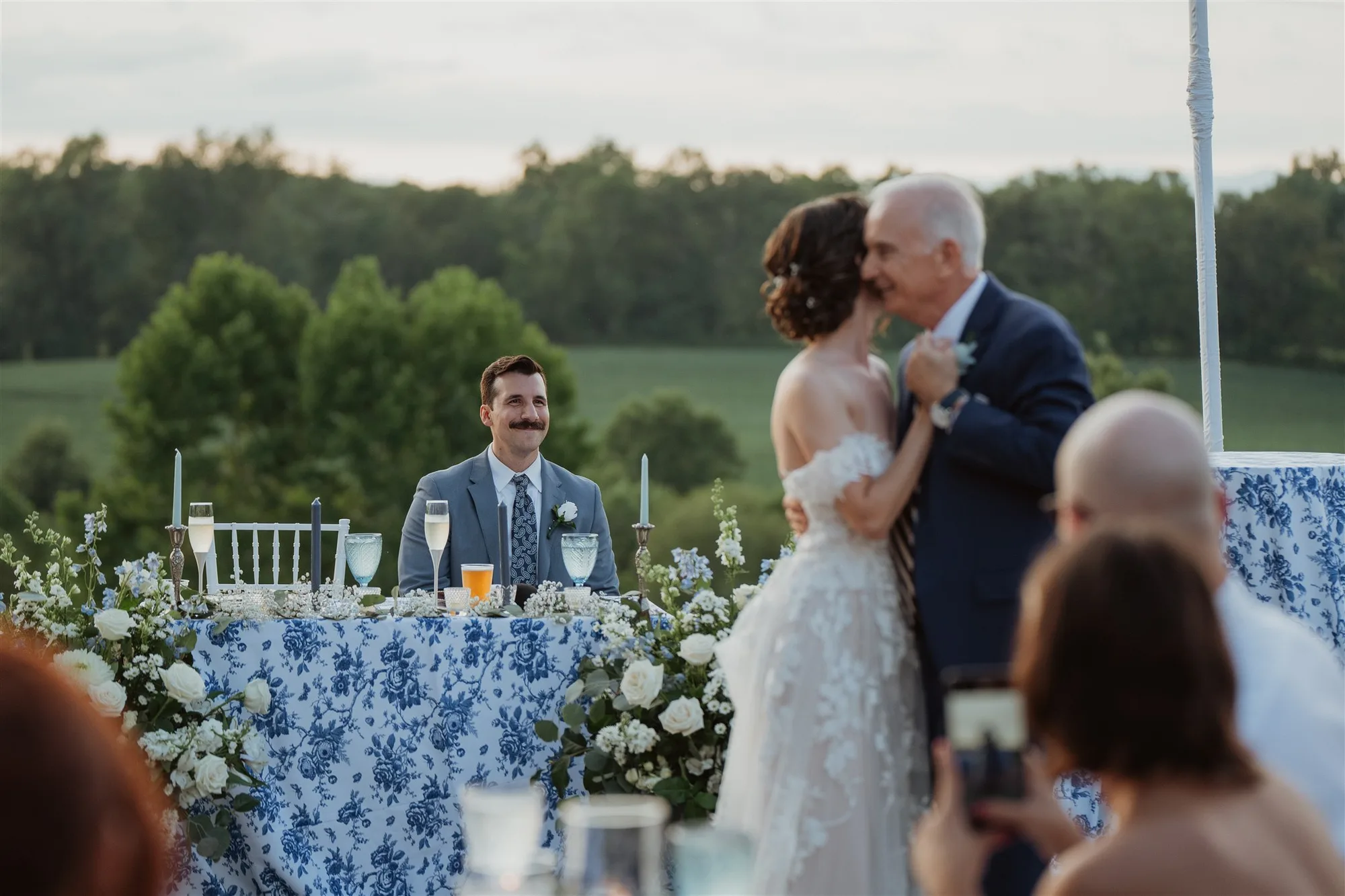 Groom watches bride dance with her father at outdoor Rixey Manor reception with rolling Virginia hills behind