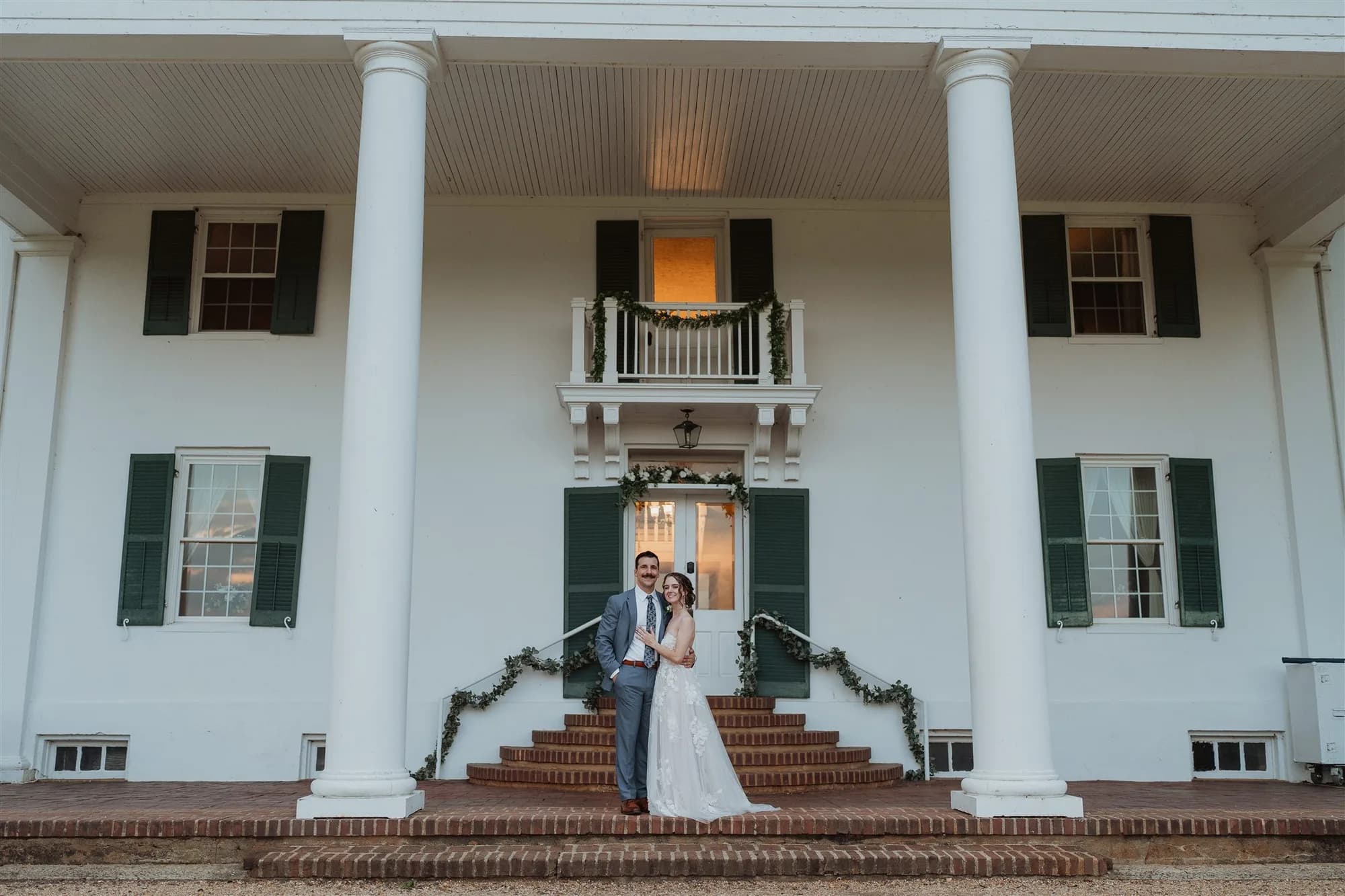 Bride and groom embrace on the brick steps of Rixey Manor's white-columned antebellum facade at dusk
