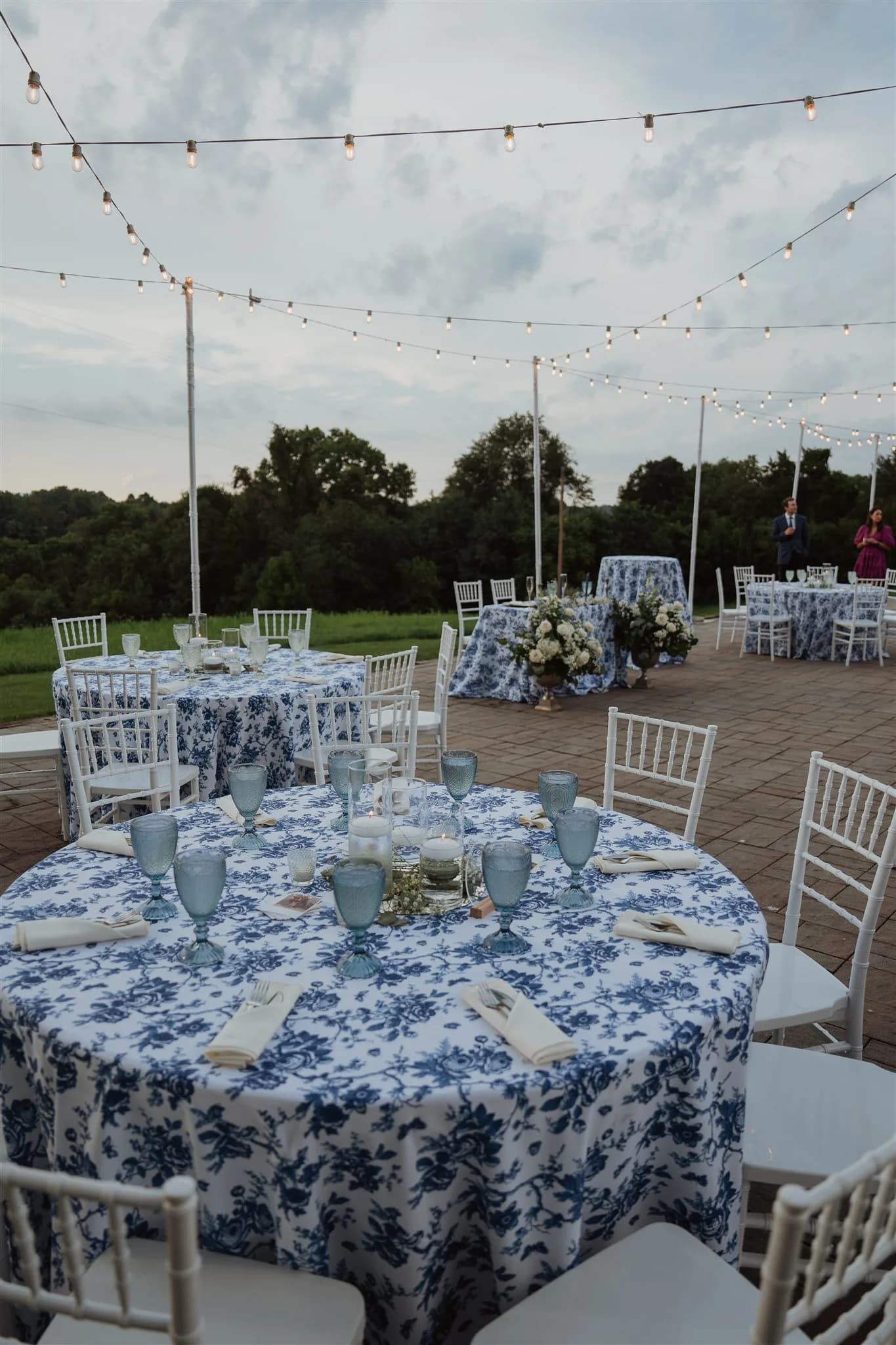 Outdoor reception tables with blue floral linens and string lights at Rixey Manor terrace at dusk