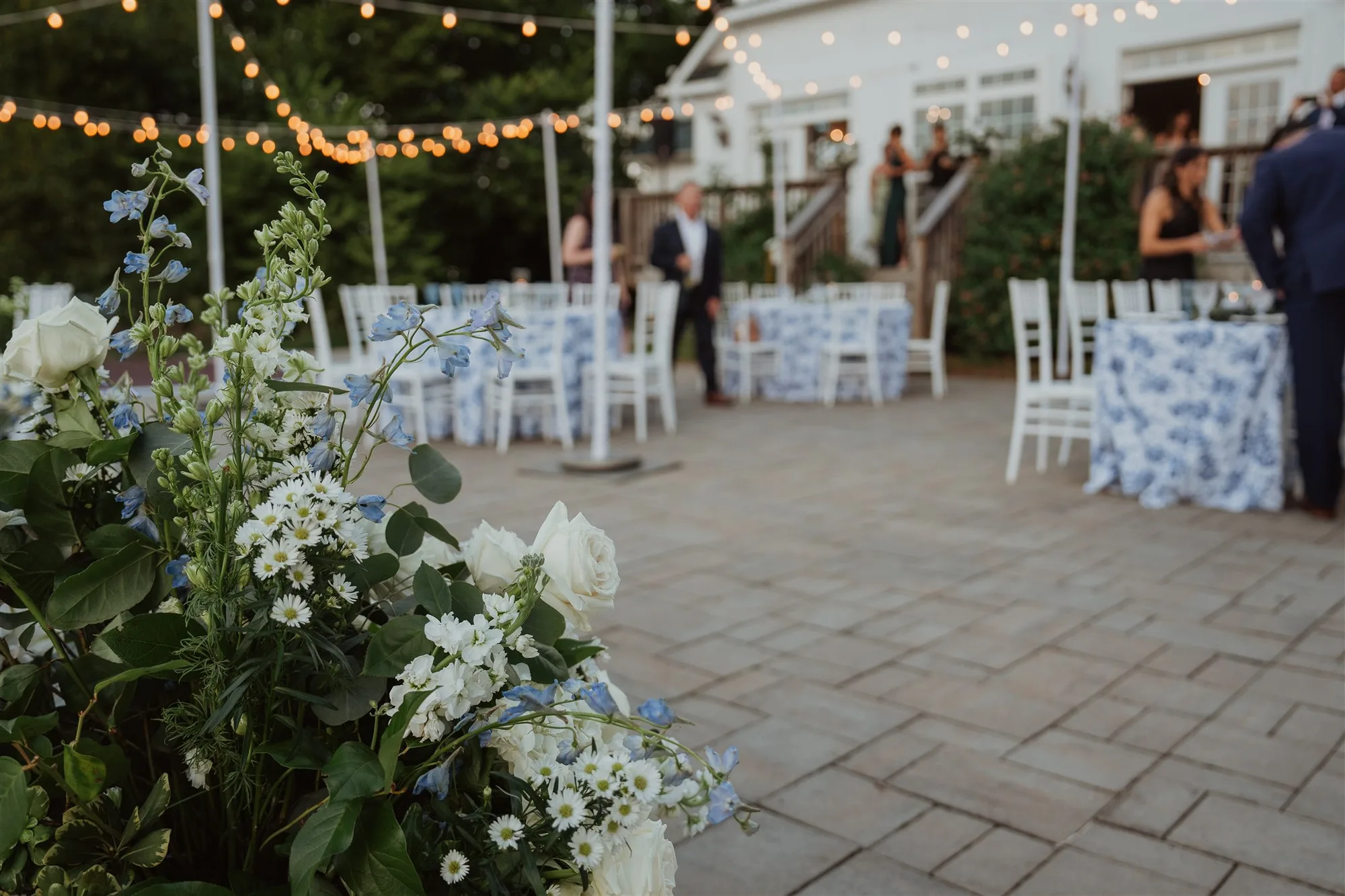 Blue floral arrangements frame a candlelit outdoor reception patio with string lights at Rixey Manor