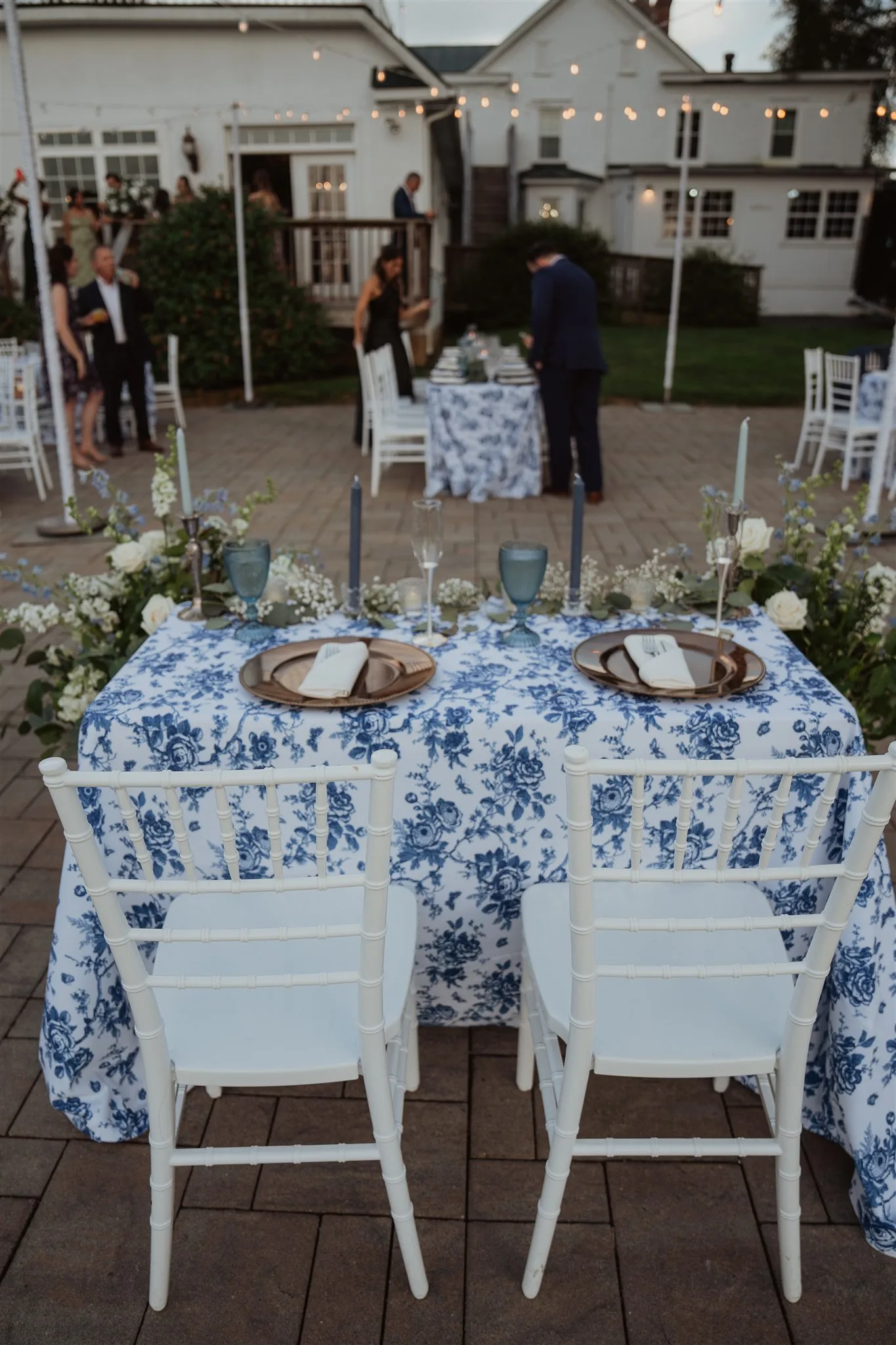 Blue floral sweetheart table with white Chiavari chairs on Rixey Manor's evening patio amid candlelight and florals