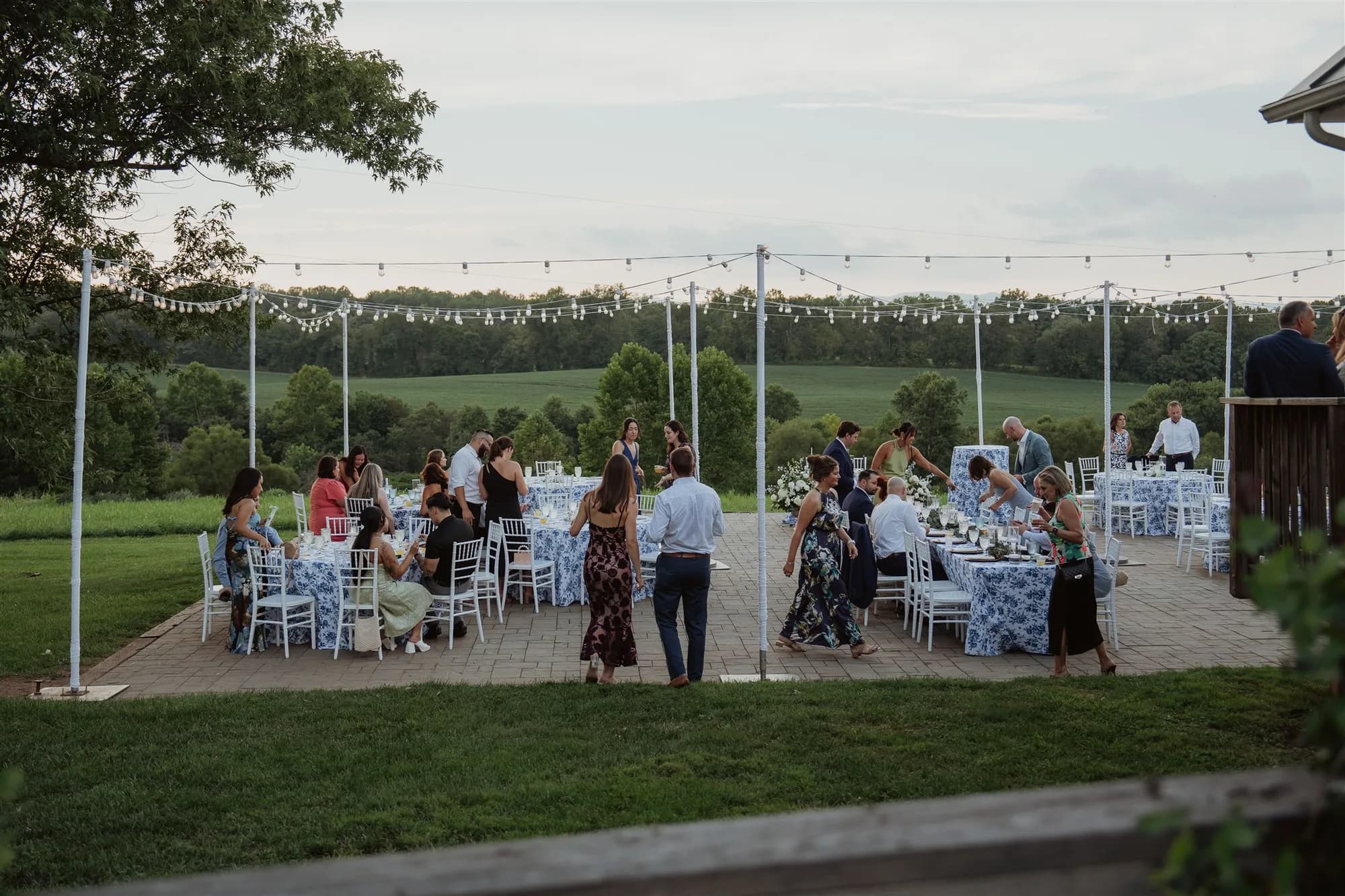 Outdoor wedding reception under string lights with guests seated at tables on manicured lawn
